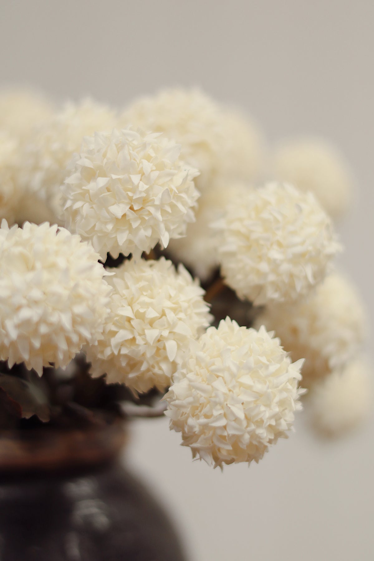 close up on a Vintage dark brown vase with MORANDI IVORY artificial flowers on a wooden surface and light gray background at la maison garçonne montreal