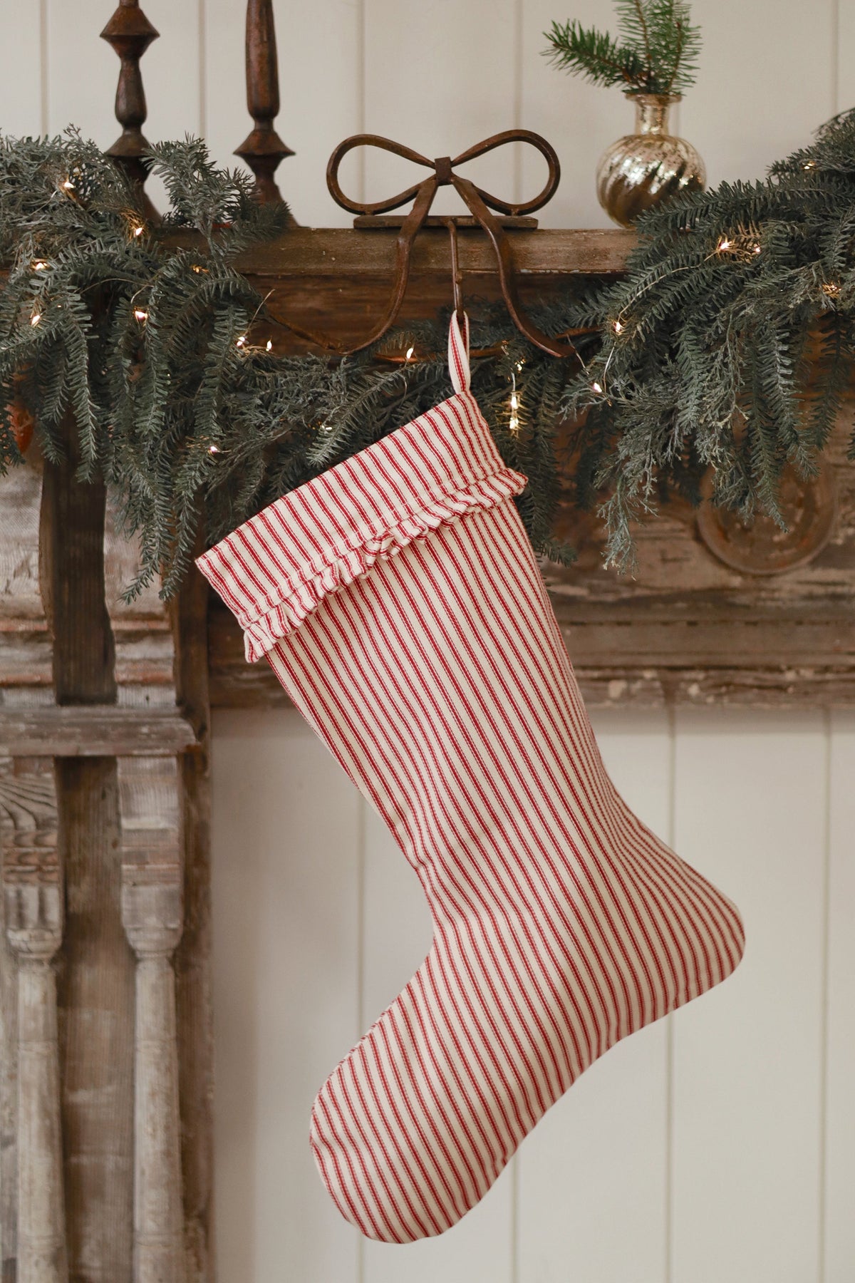 Red and white striped Christmas stocking hanging on a wooden mantel with greenery at maison garçonne montreal.