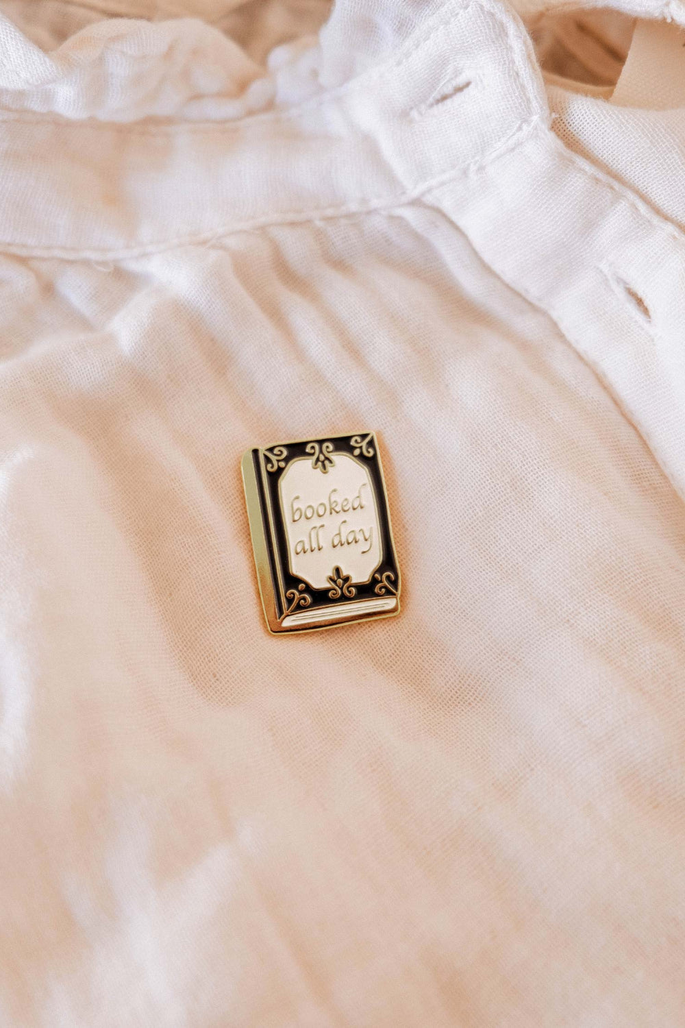 Enamel Pin with 'booked all day' text from Mimi and August on a textured surface