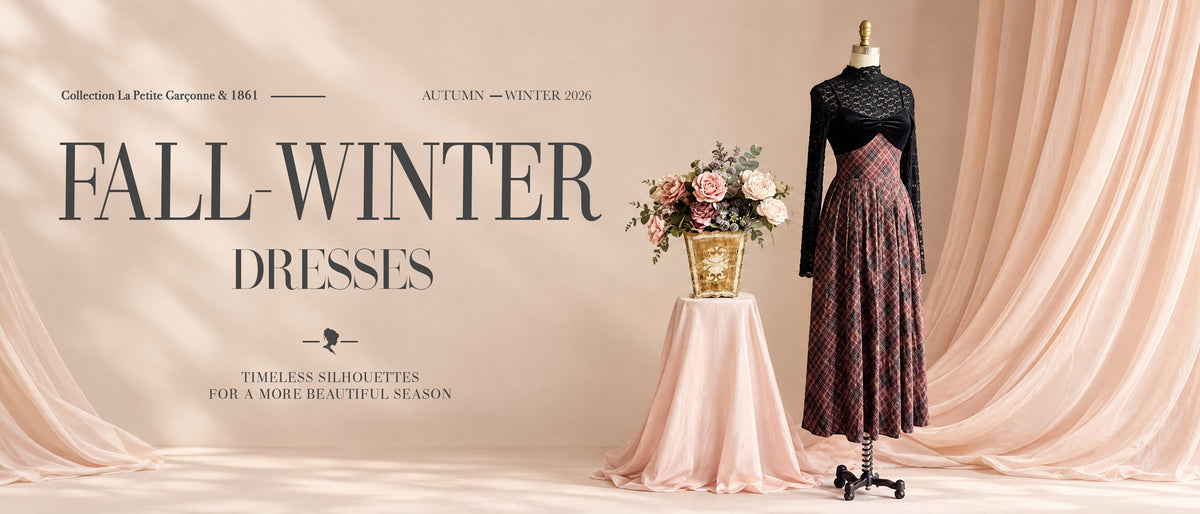 A fashion promotional banner for fall-winter dresses, featuring a long-sleeve black lace top paired with a dark patterned pleated skirt displayed on a mannequin, alongside a matching light pink draped tablecloth and floral arrangement against a soft beige backdrop with draped fabric at boutique 1861 in Montreal.