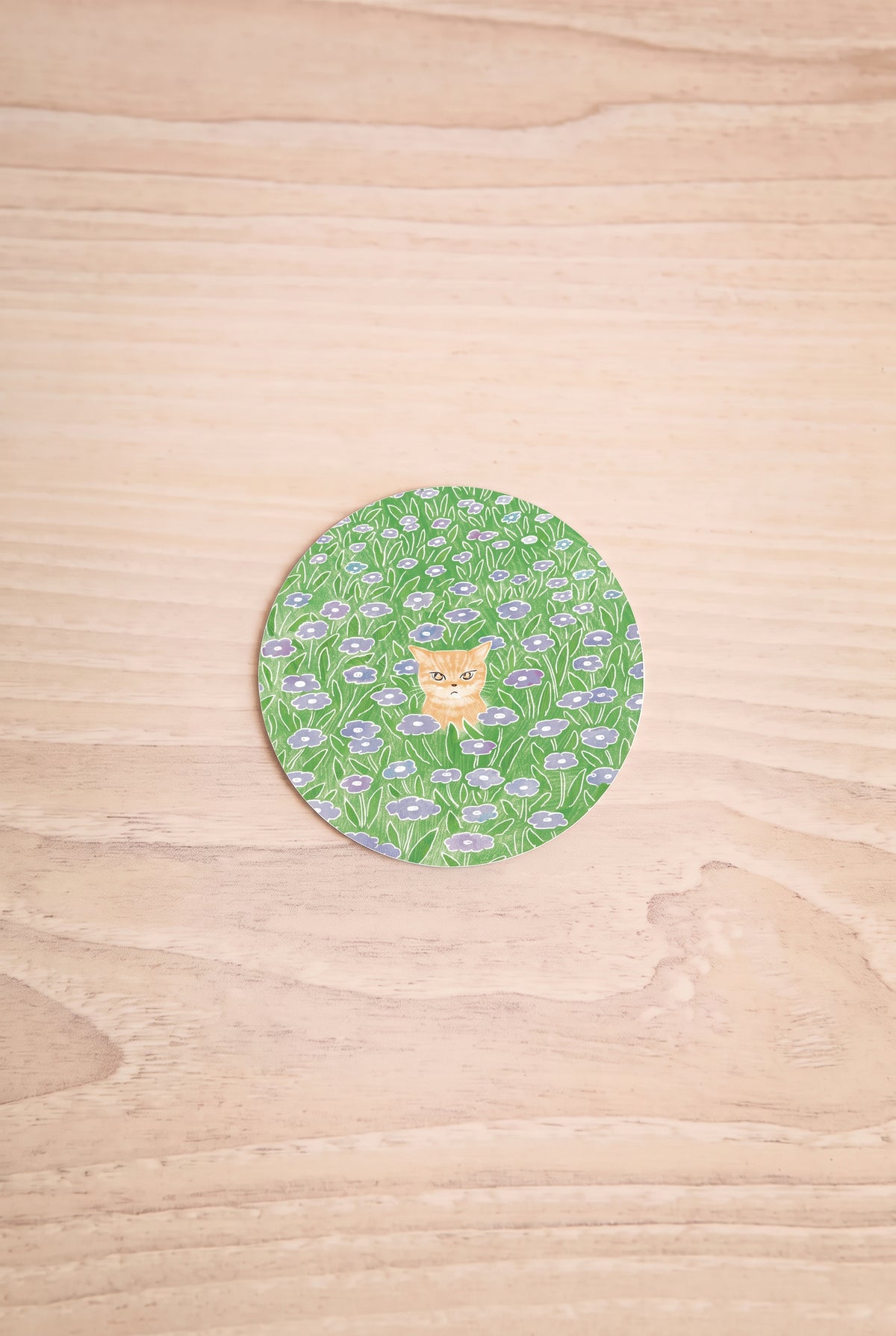 A round sticker featuring a green and white floral pattern with a small orange cat in the center, illustrated by Foonie at la maison garçonne montreal