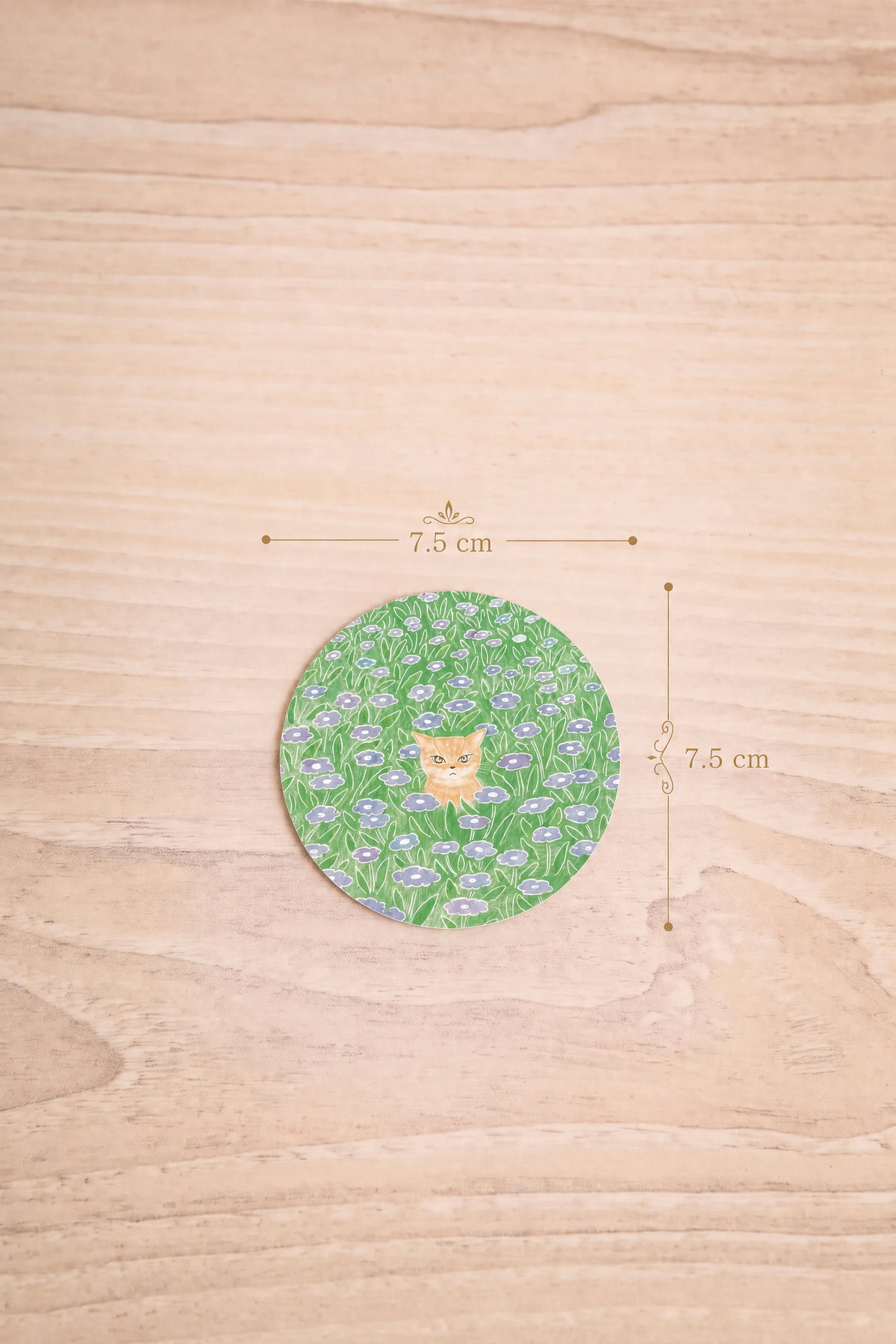dimension 7.5cm x 7.5 cm of a round sticker featuring a green and white floral pattern with a small orange cat in the center, illustrated by Foonie at la maison garçonne montreal