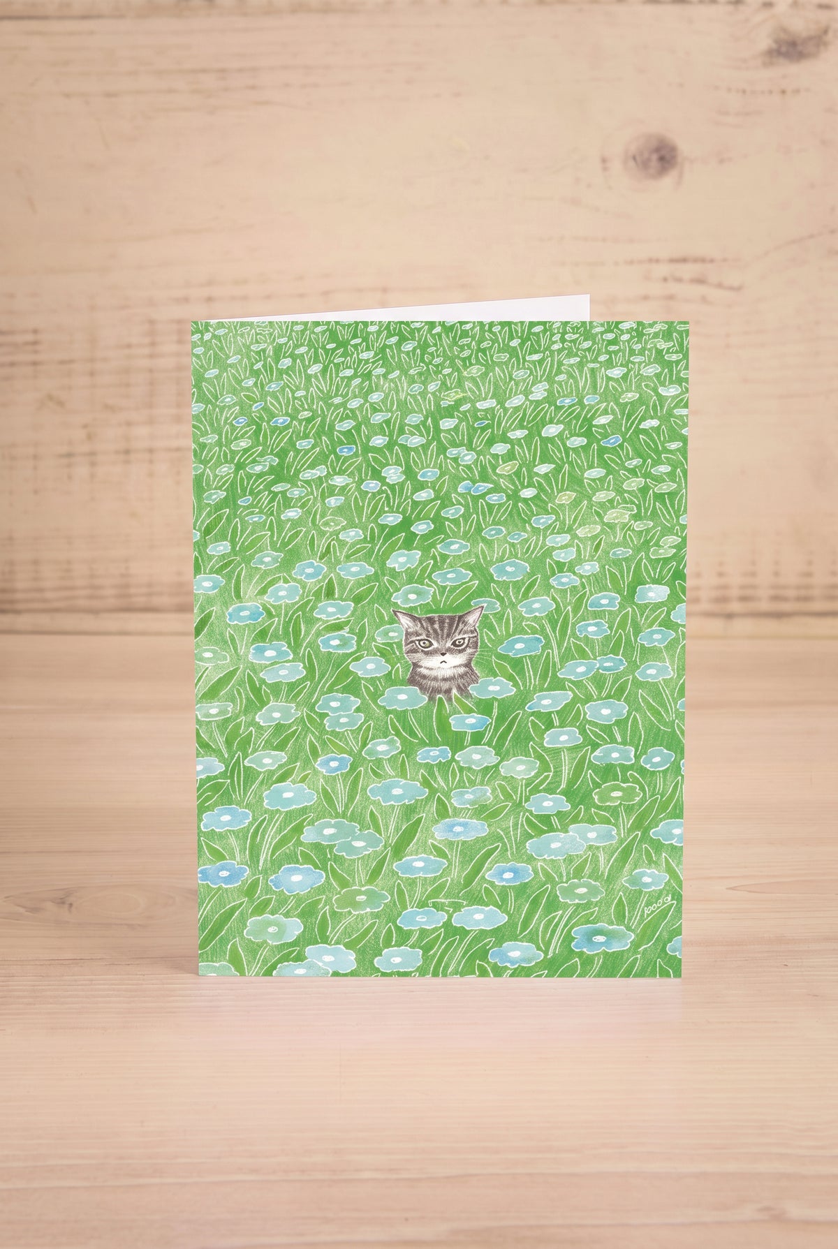 A vertical greeting card featuring a watercolor-style green field of flowers with a small tabby cat by Foonie at maison garçonne in montreal