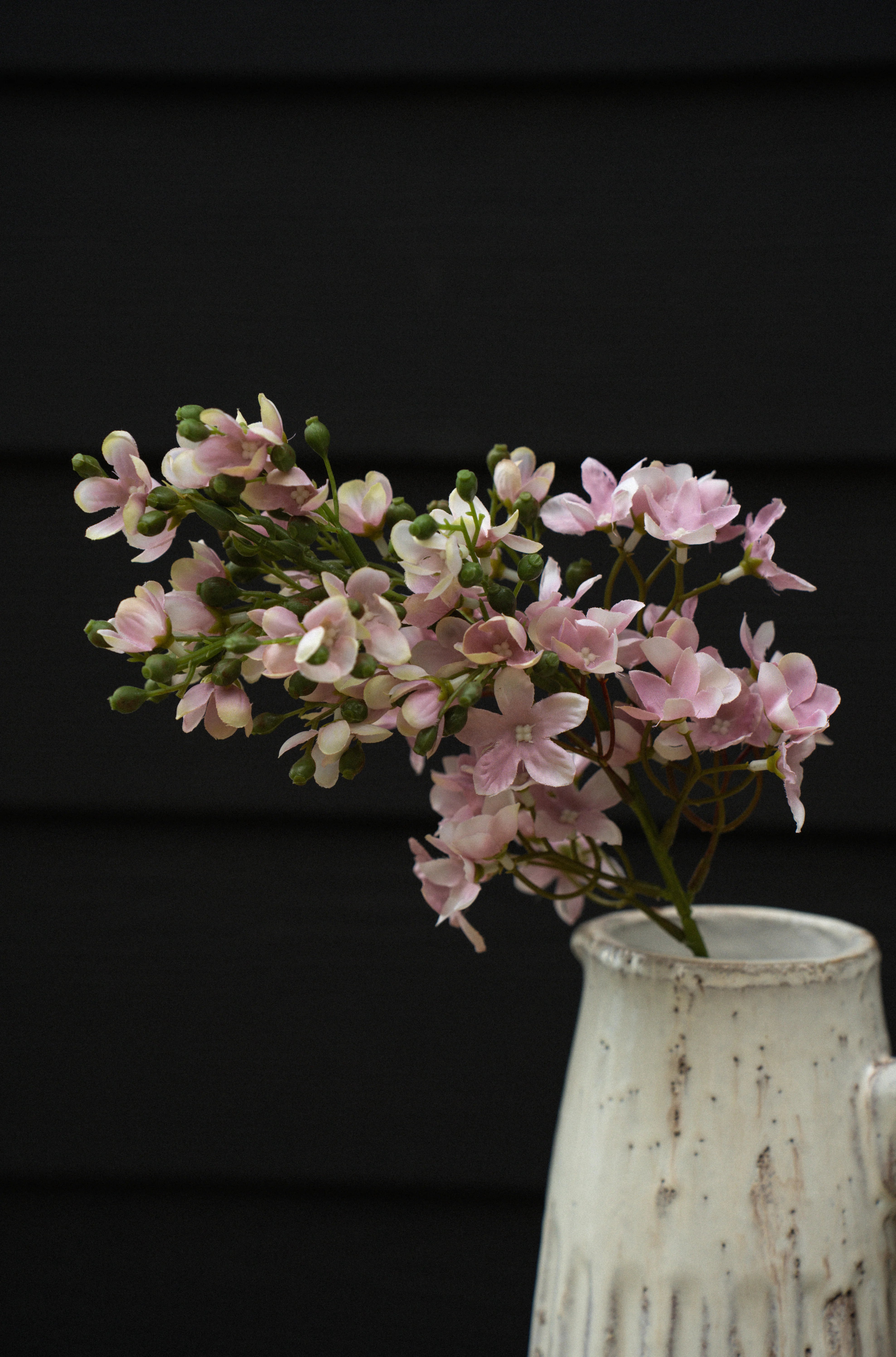 Delphinium Floral Stem in pink in a rustic white vase against a dark background