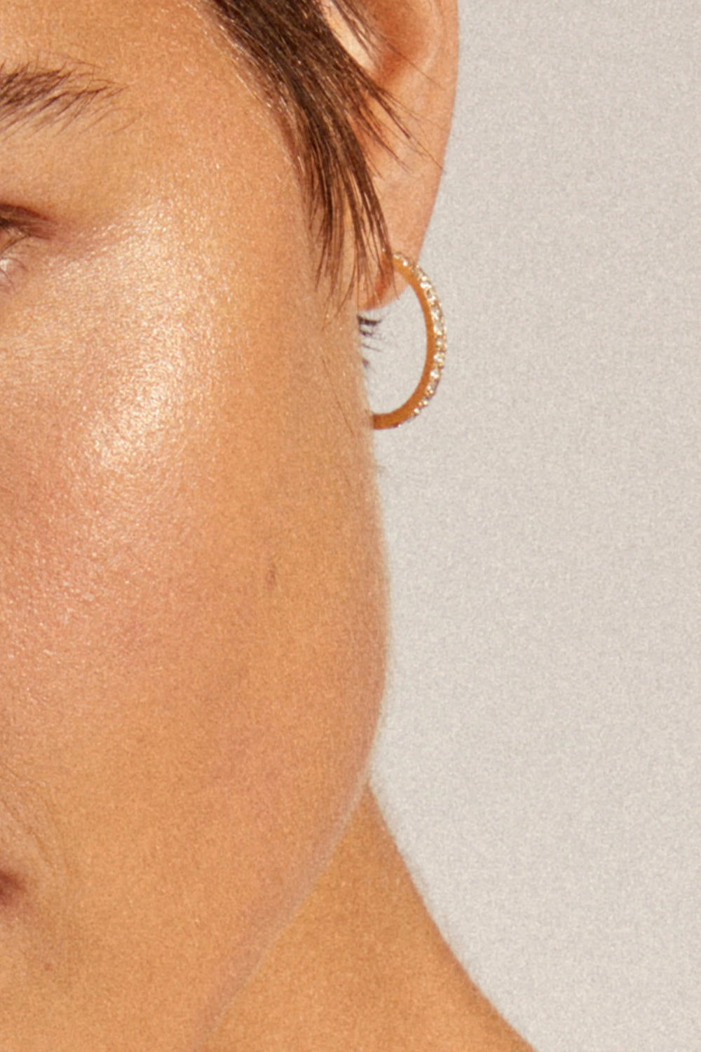Close-up of a woman wearing Ebna gold from Pilgrim, a gold hoop earring with stone details