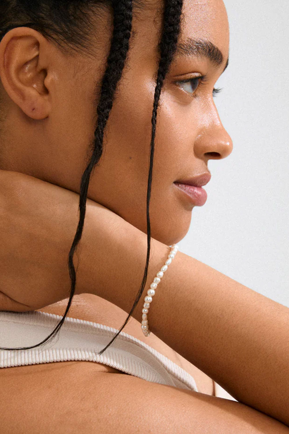 Close-up of a woman with braided hair wearing a pearl necklace EXETER-GOLD by Pilgrim against a neutral background
