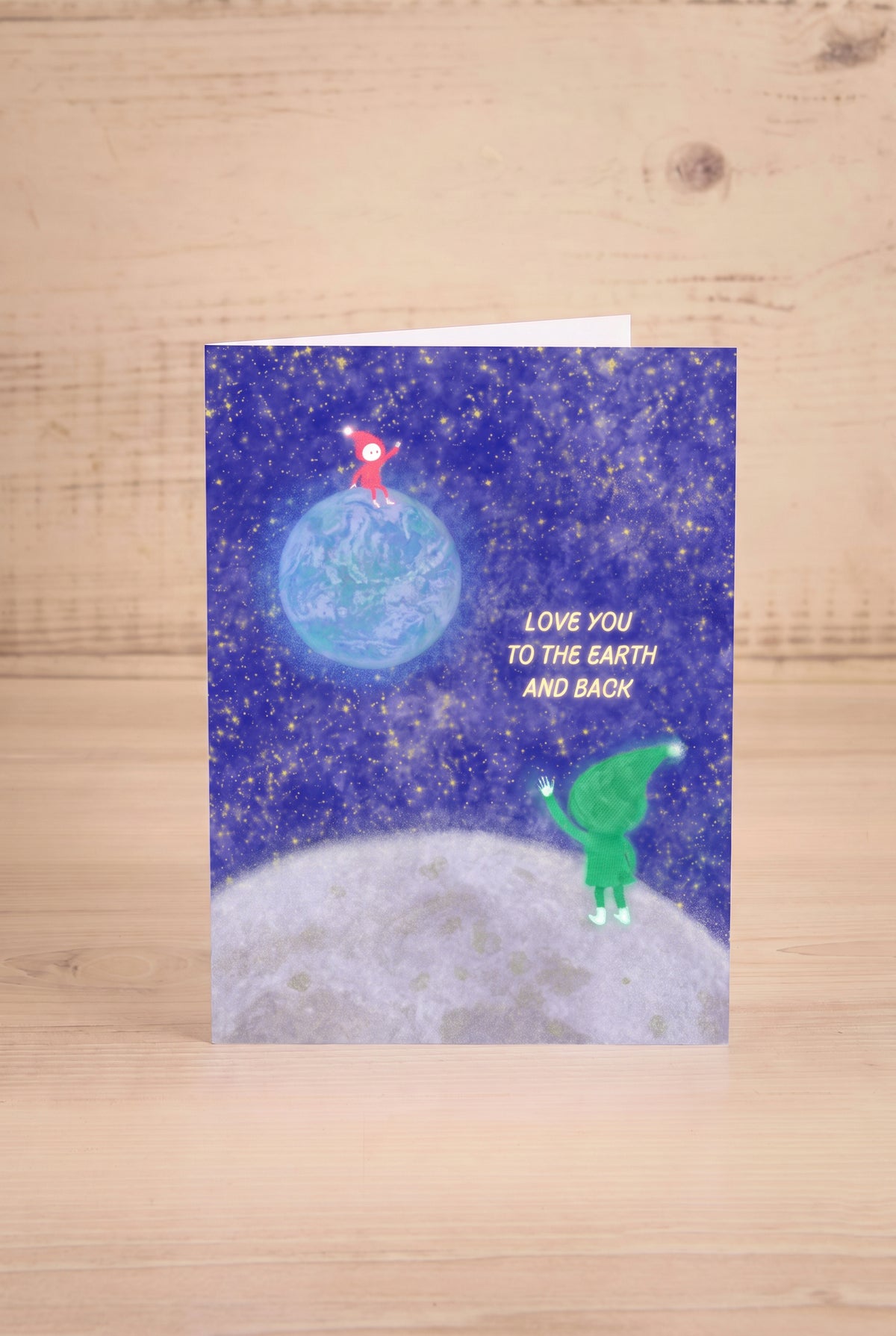 A greeting card featuring a space-themed illustration with the text 'LOVE YOU TO THE EARTH AND BACK'. illustrated by Foonie at la maison garçonne montreal