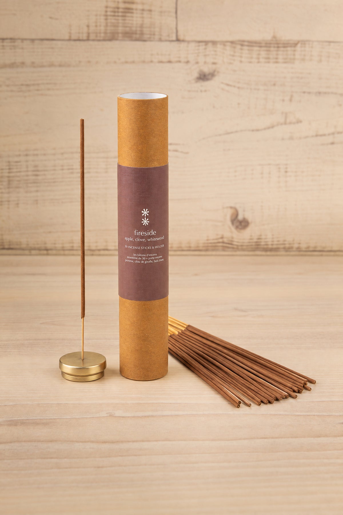 A tube of incense sticks with a matching incense holder and several incense sticks fanned out on a light wood background. The tube has a brown paper finish with a dark mauve label and the brand name 'Lemnide' is visible at la maison garçonne in montreal