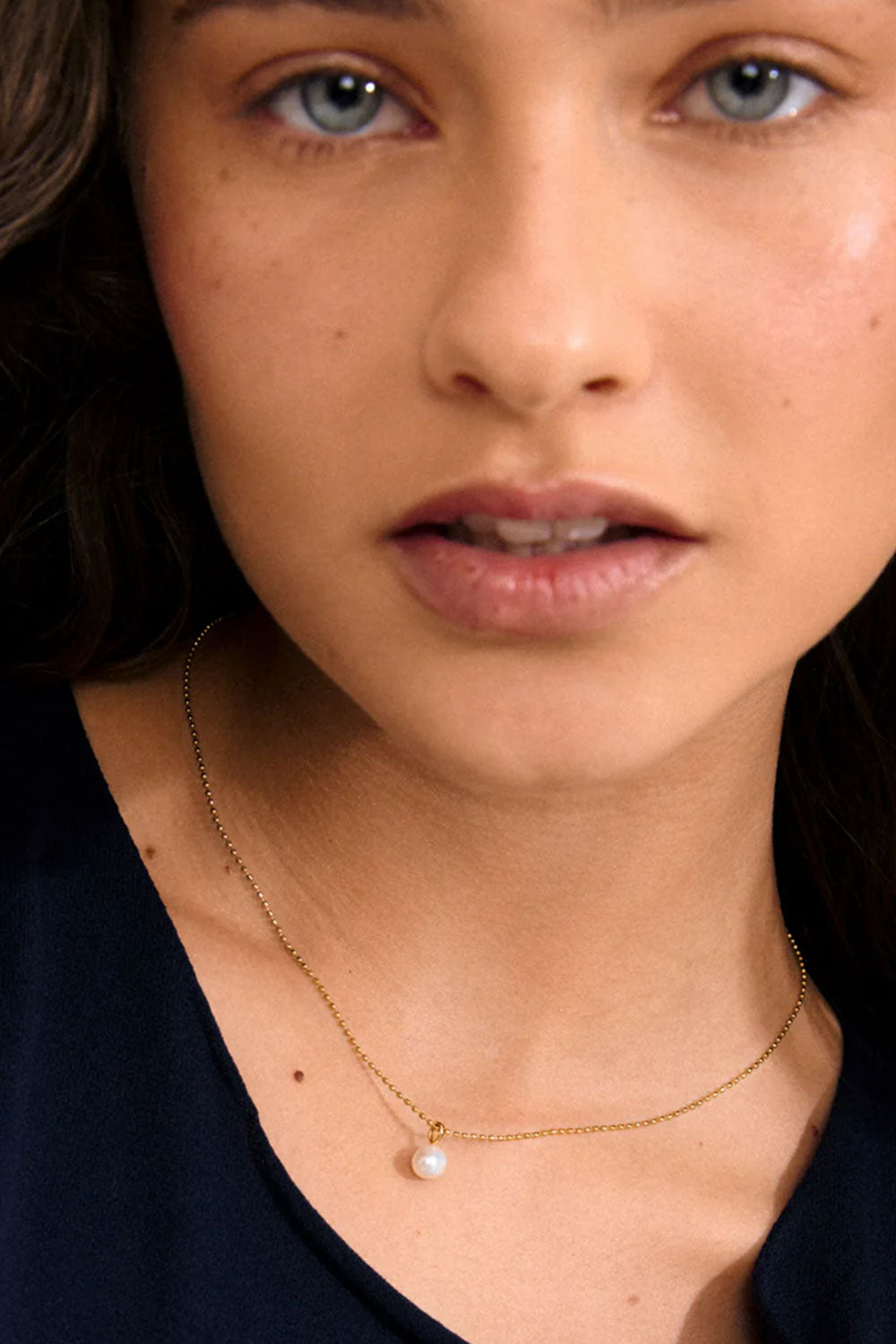 Close-up of a person wearing a gold necklace GUIDEL-GOLD by Pilgrim with a pearl pendant.