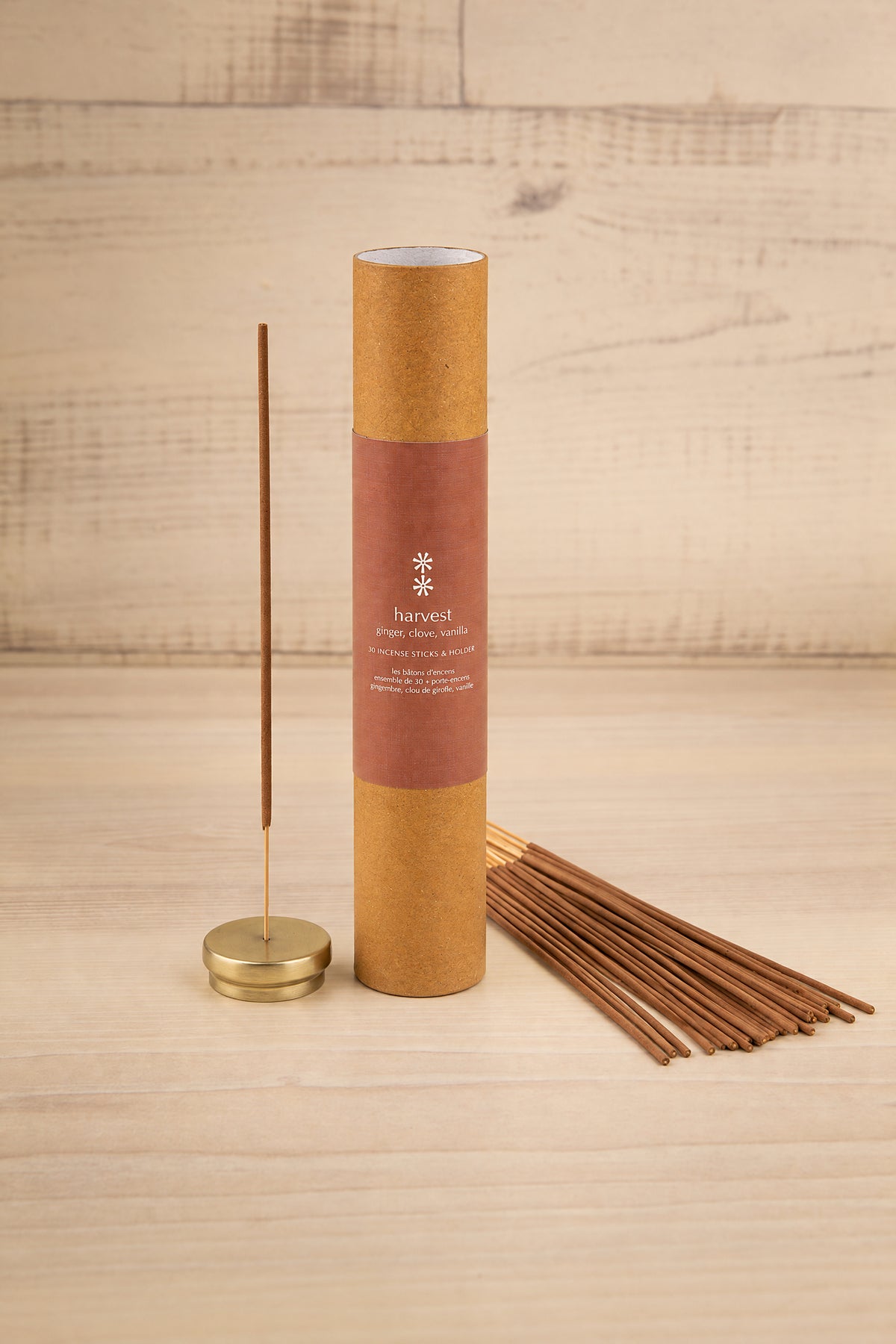 A tube of incense sticks with one stick standing upright in a brass holder, with several incense sticks fanned out beside it on a light wood surface at la maison garçonne in montreal