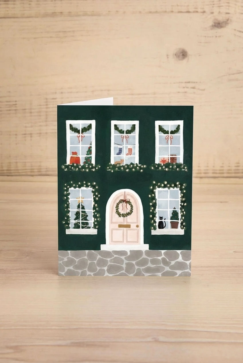 Christmas-themed greeting card from Mimi & August with a house facade, windows, and door decorated with lights and wreaths on a green background.