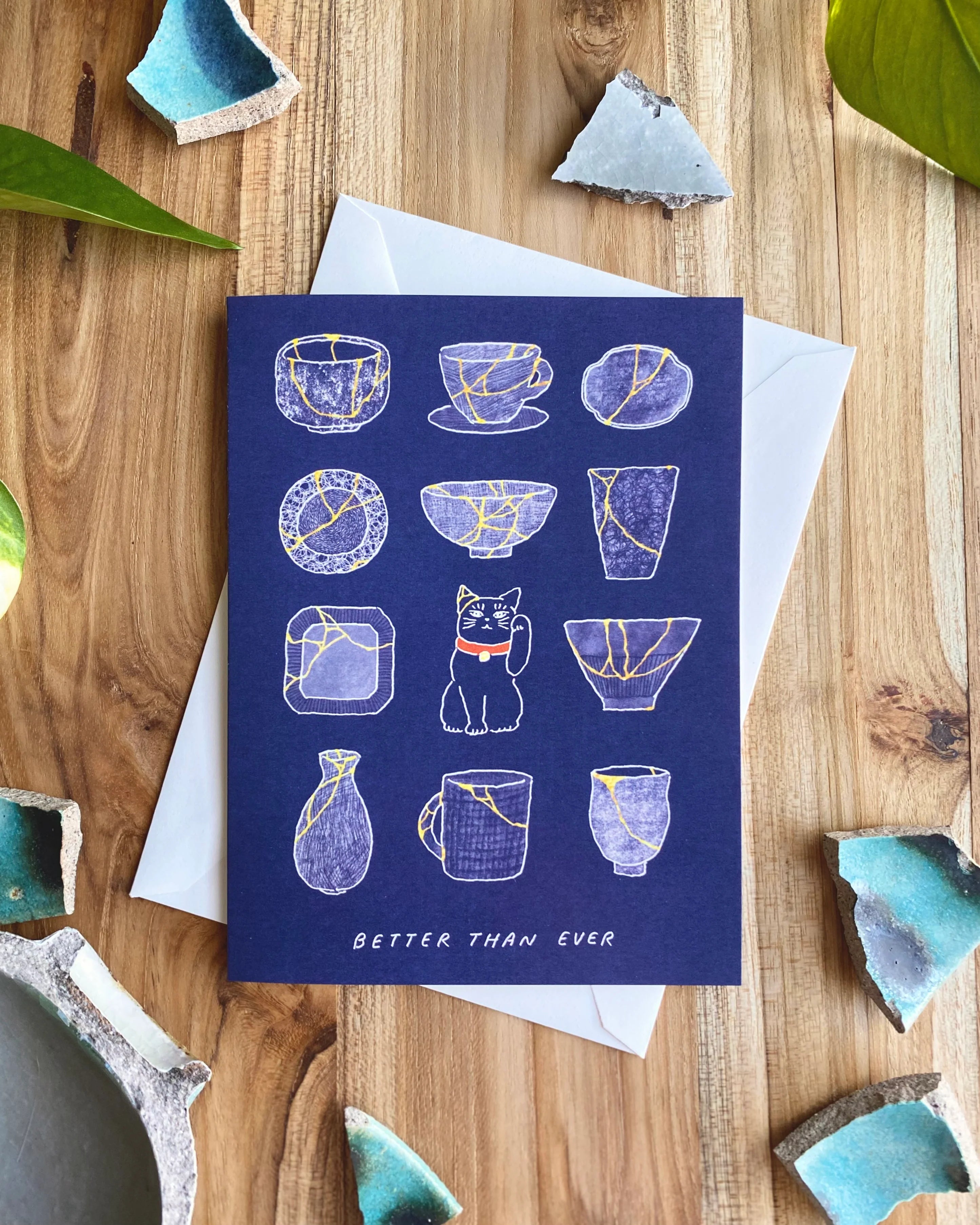 Greeting card with illustrations of ceramic items on a wooden surface with broken ceramic pieces.
