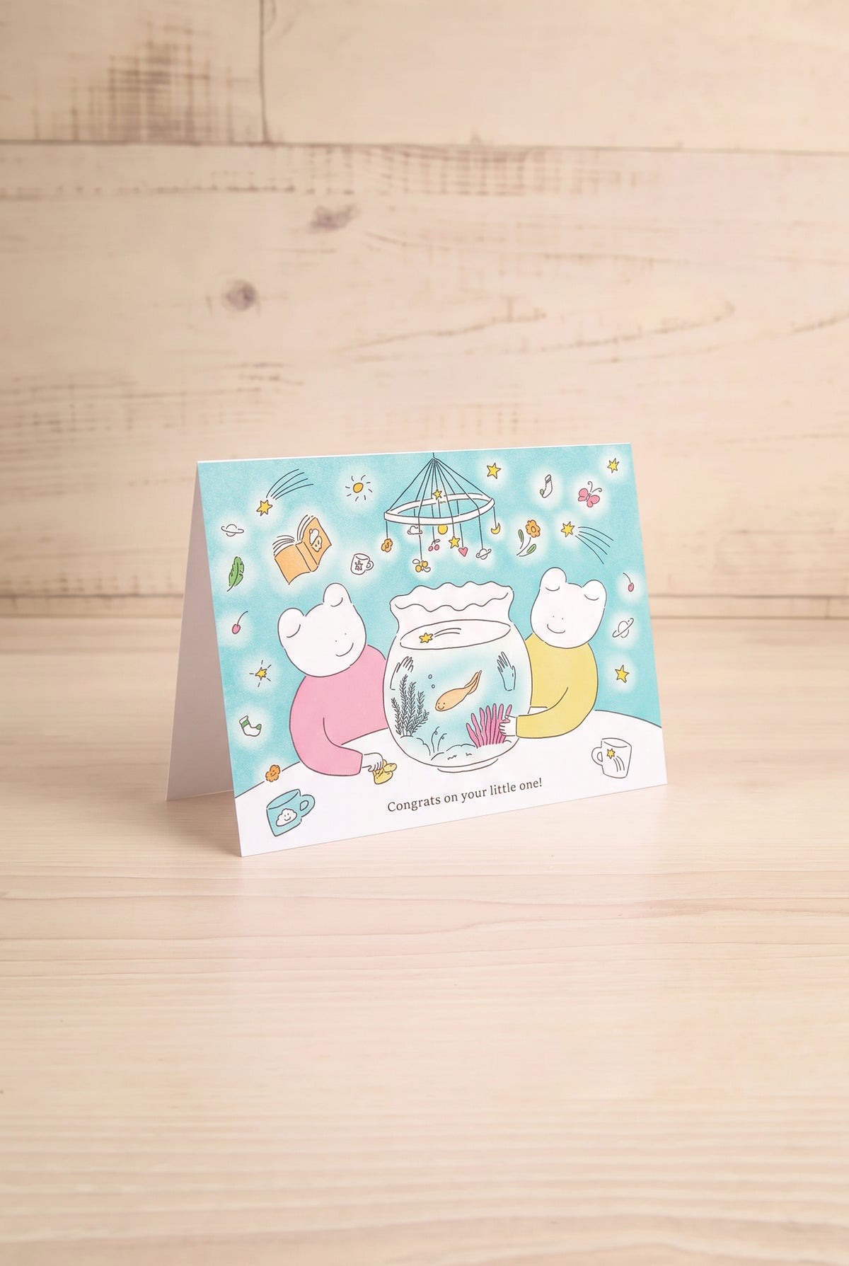 A small illustrated greeting card by foonie showing two cartoon bears around a fishbowl with a blue watermelon-patterned background and the text 'Congrats on your little one!'. at la maison garçonne montreal