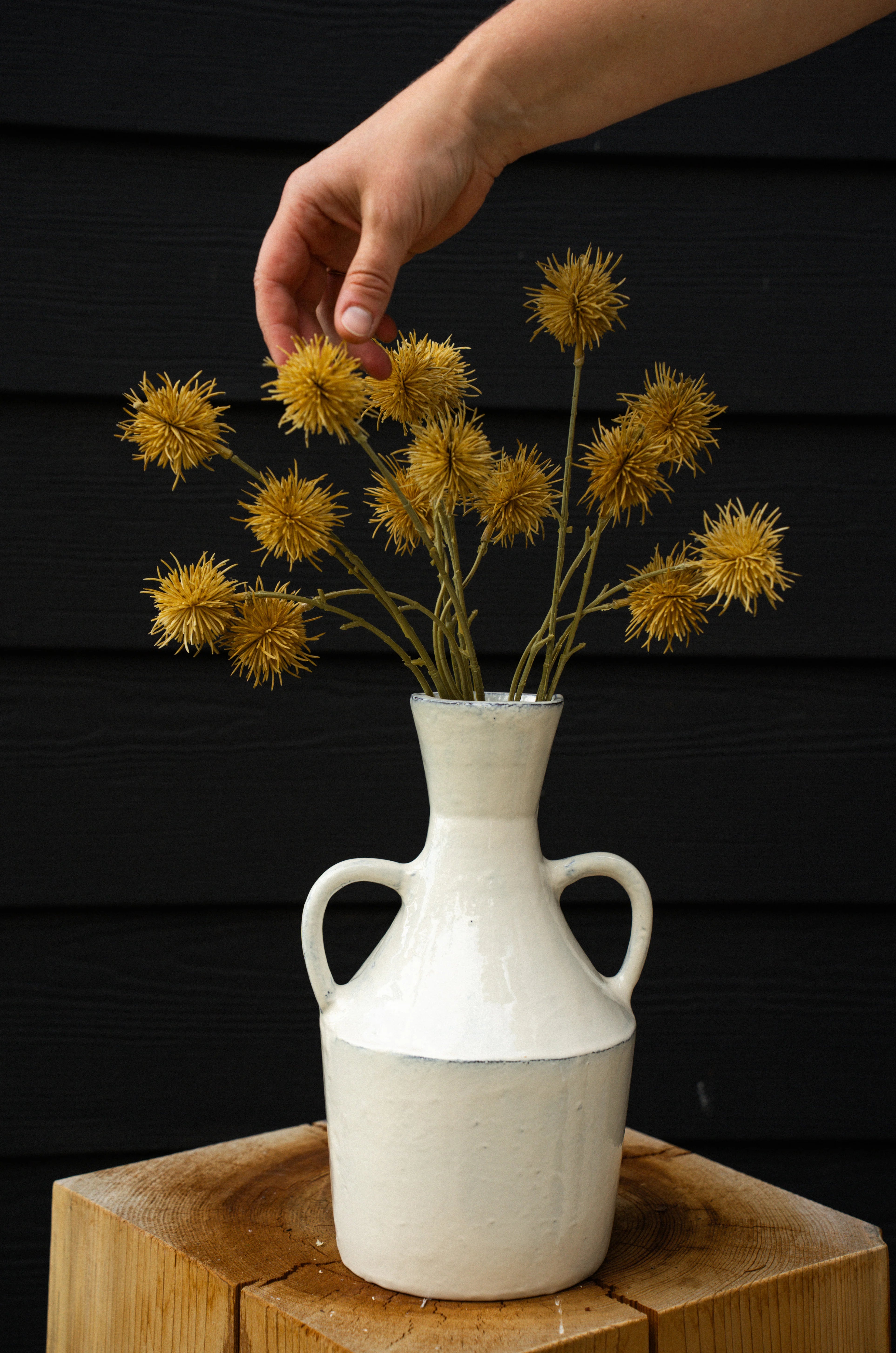 White vase with Chestnut Ball flower Bouquet in Light Brown on a wooden surface against a black background