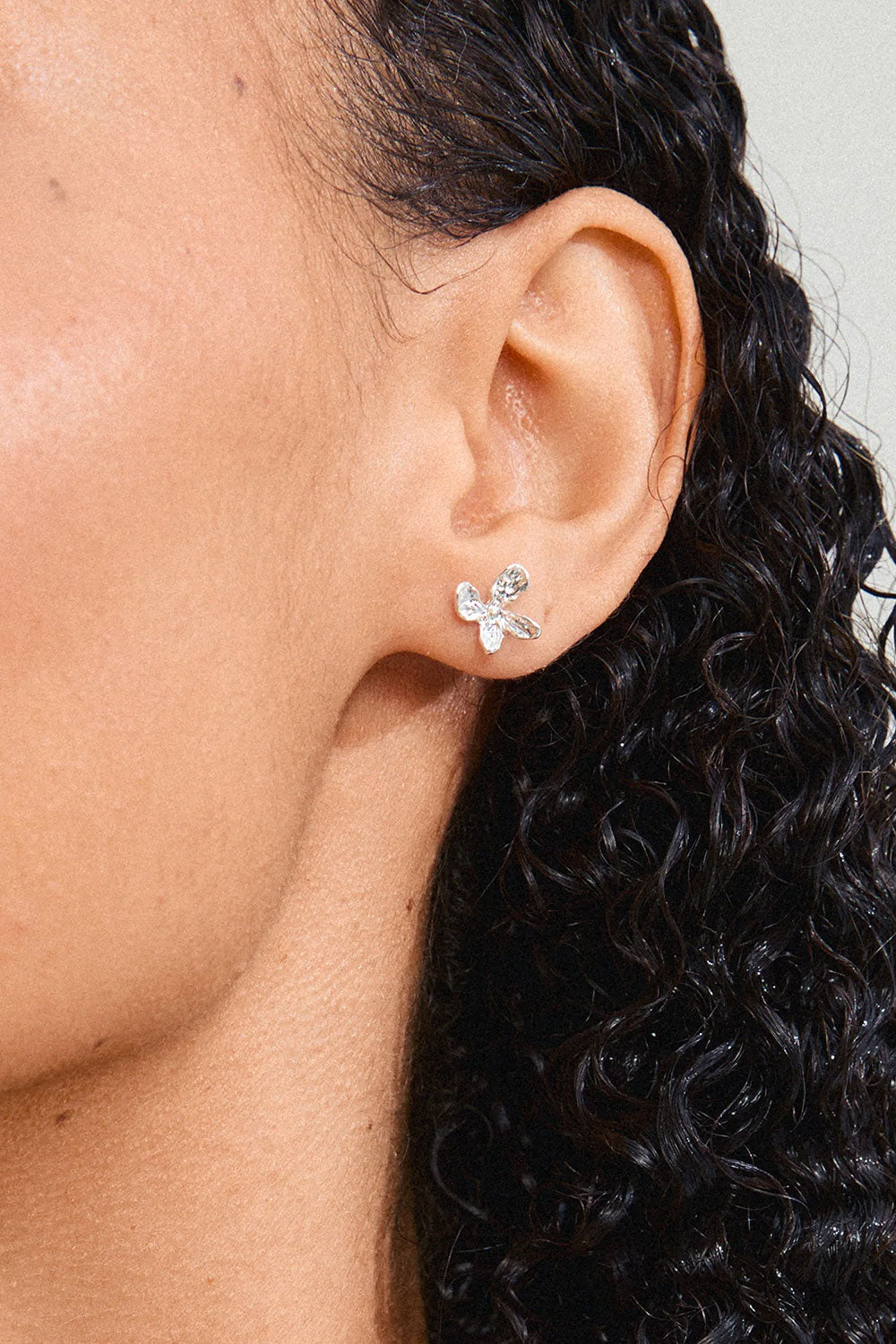 Close-up of a woman wearing a silver flower-shaped AGLAIA earring from Pilgrim La petite garçonne Montreal