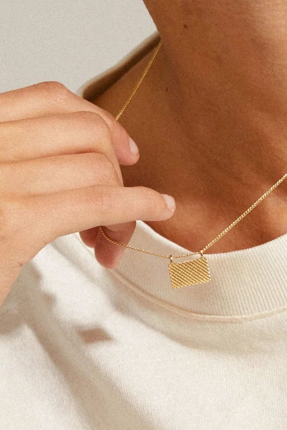 Pulse from Pilgrim, a gold necklace with a geometric pendant worn by a person. Available at la petite garçonne in Montreal