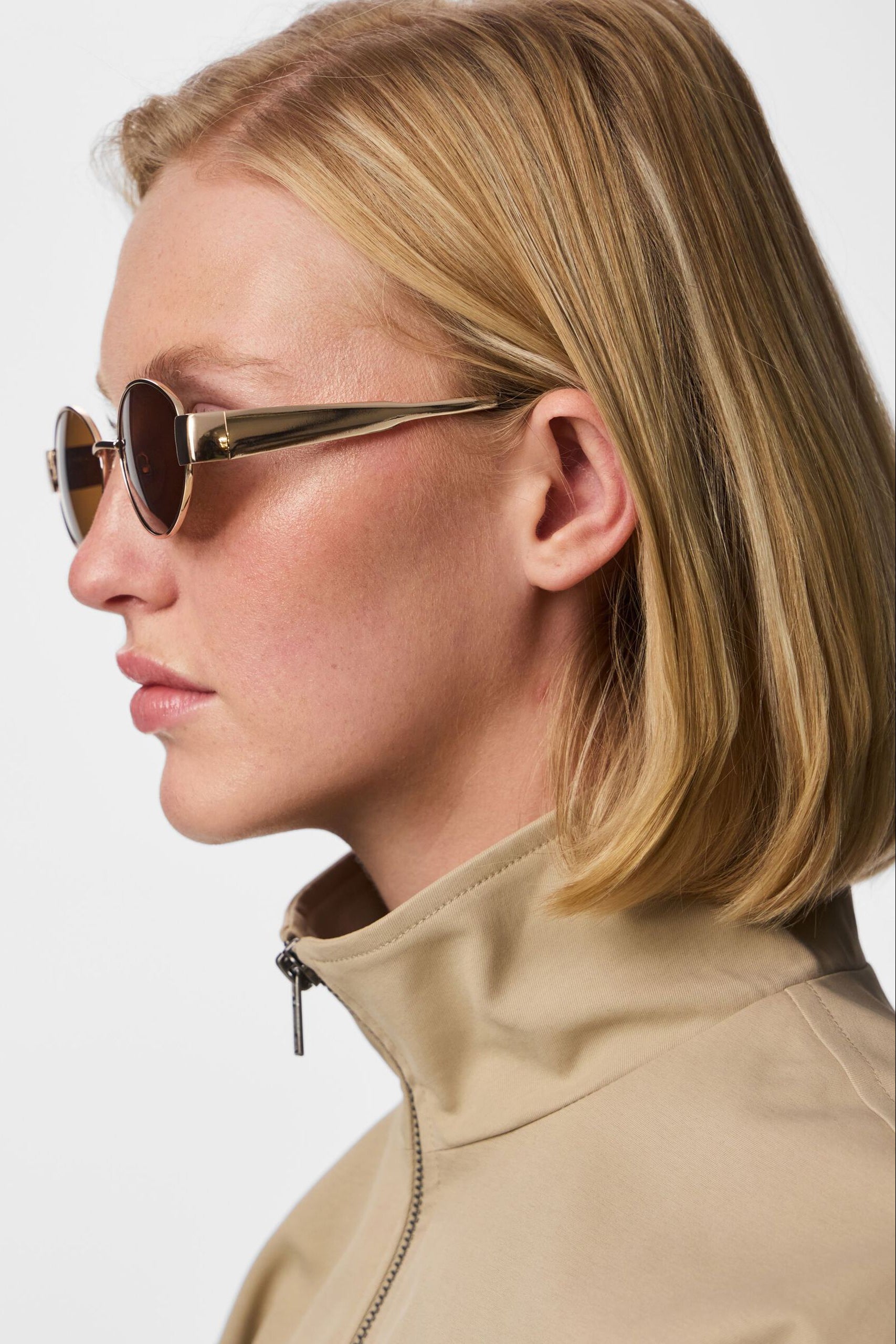 profile woman wearing Solstice Gold Oval Sunglasses with Brown Lenses