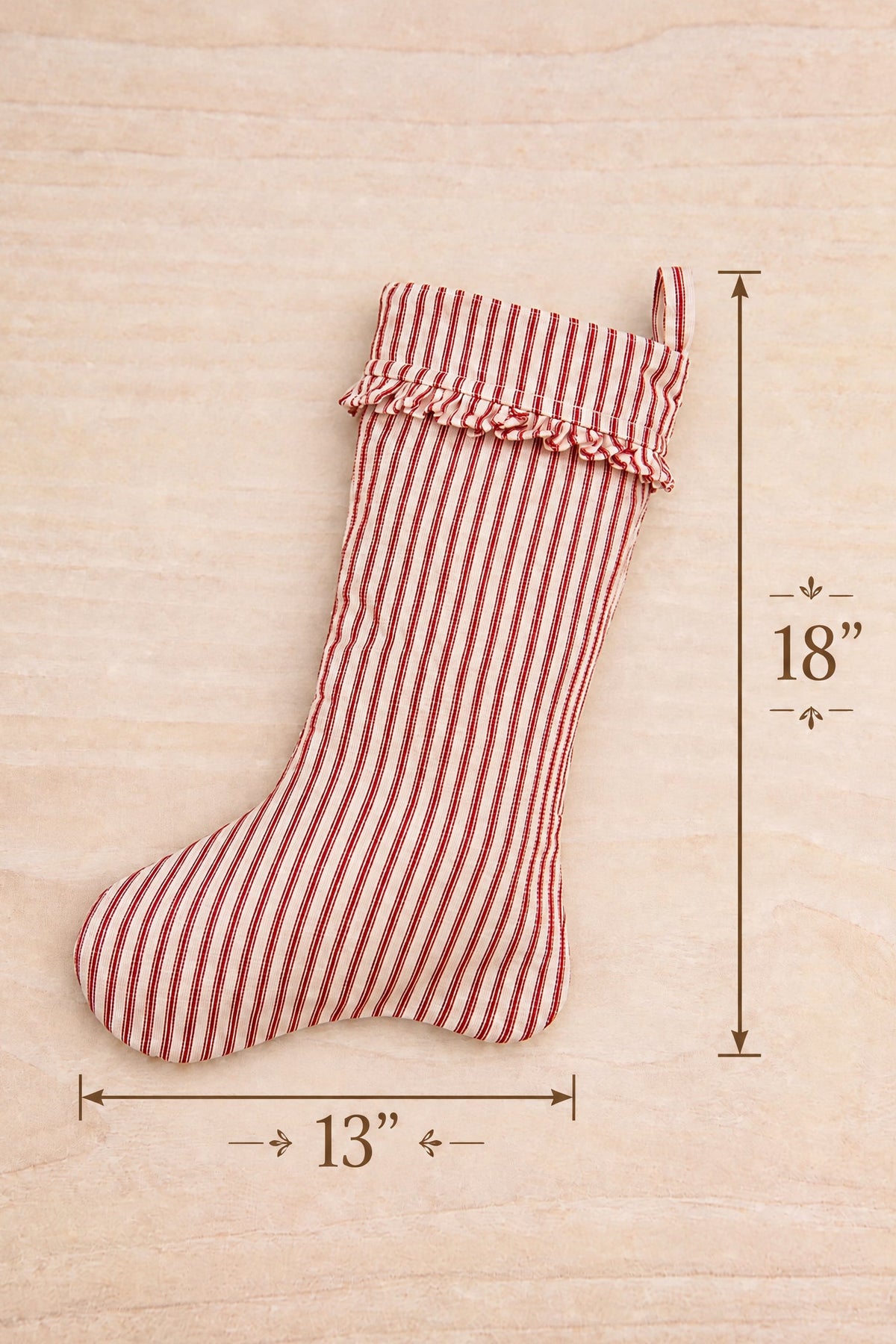 A red and white striped fabric Christmas stocking shown on a light wood background at la maison garçonne in montreal with dimension lines indicating 13 inches wide and 18 inches tall.