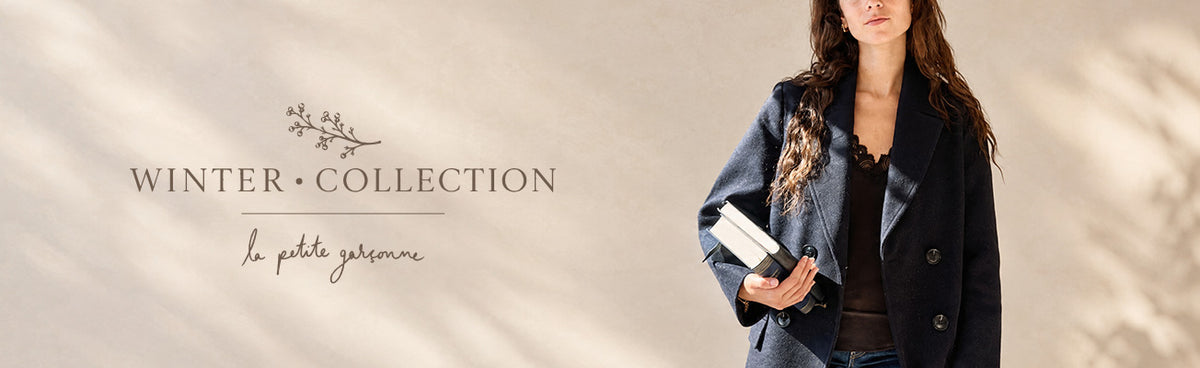A woman wearing a dark navy double-breasted coat and holding a white book, standing against a warm beige background with leaf shadows. On the left, the text 'WINTER COLLECTION available at la petite garçonne in montreal' is displayed.