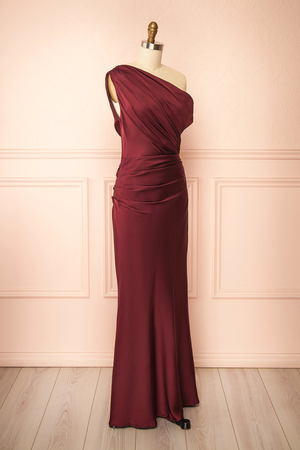 side view of mannequin wearing Colleen Burgundy Asymmetrical Satin Dress from boutique 1861
