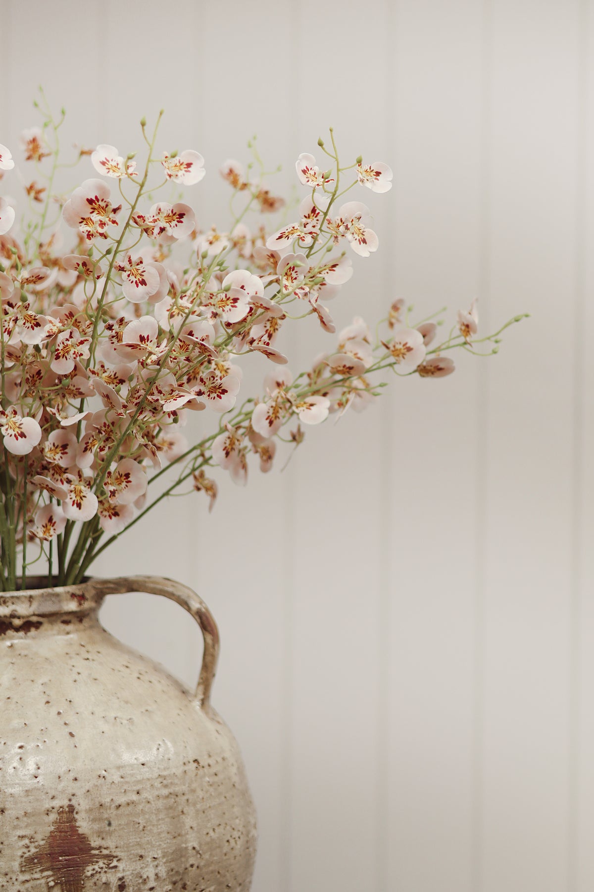 close-up on a bouquet of artificial light pink wild orchid spray flowers with green stems into a vase, on a white wood background at la maison garçonne in montreal.
