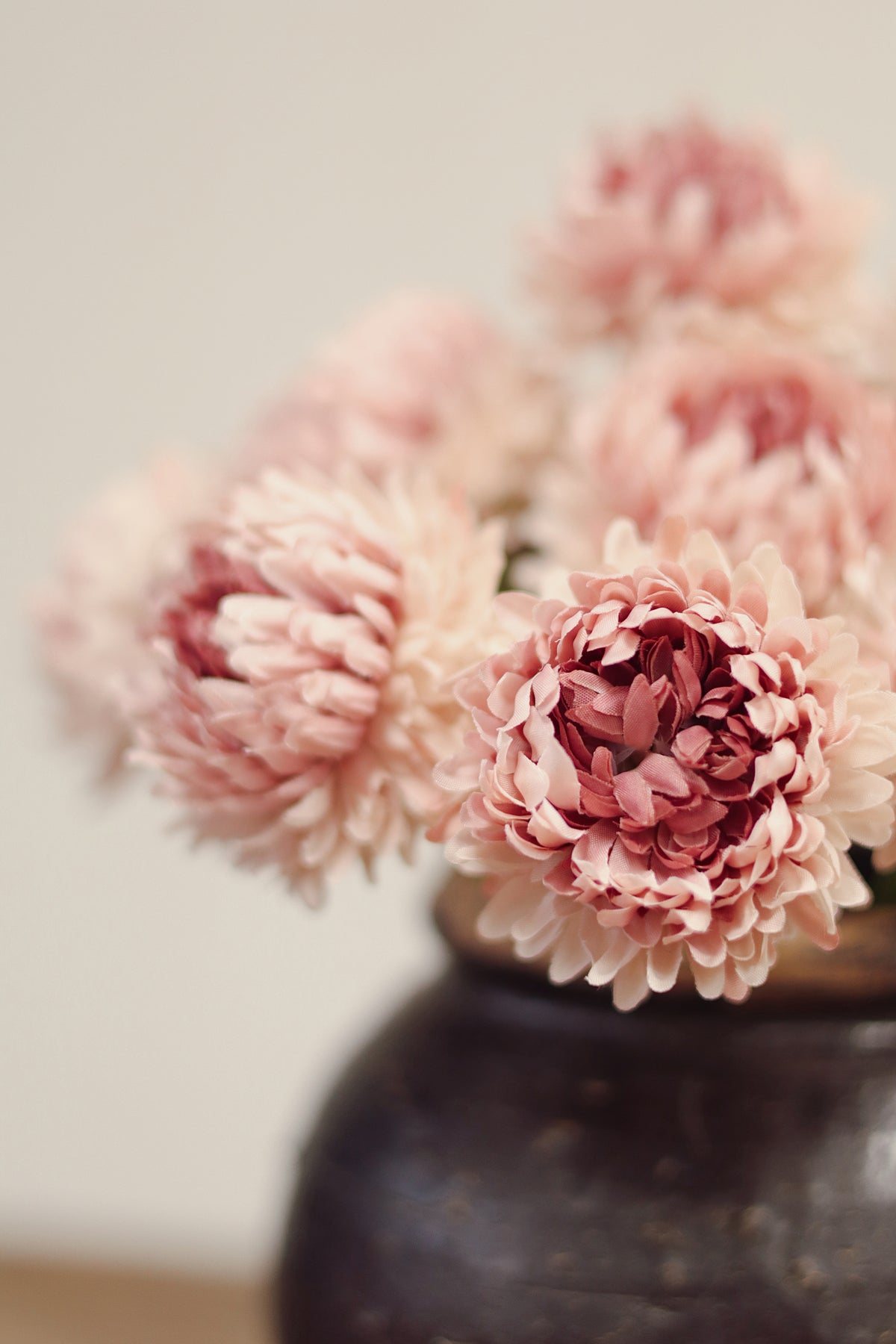close up on a Vintage-style vase with pink chrysanthemum-like artificial flowers tied together on a wood surface at la maison garçonne in montreal.