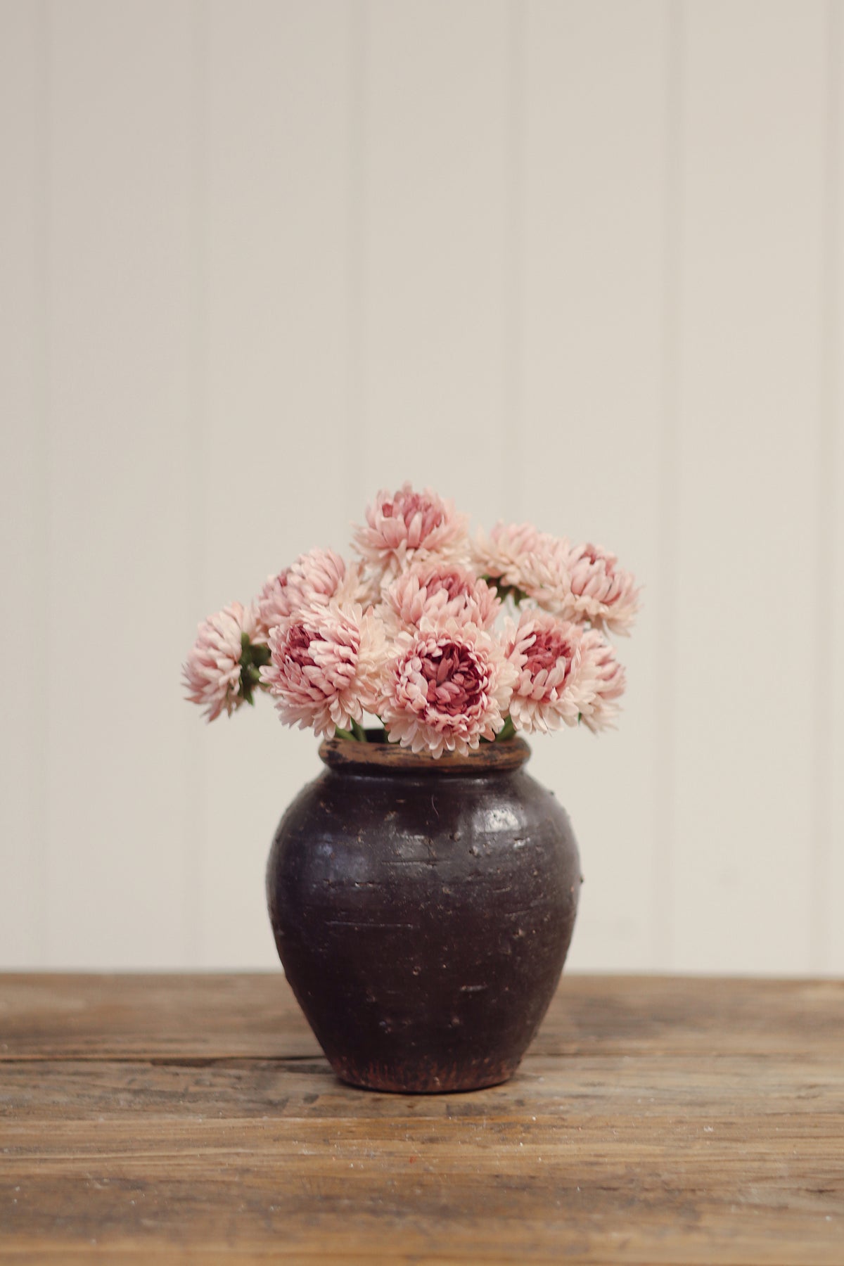 Vintage-style vase with pink chrysanthemum-like artificial flowers tied together on a wood surface at la maison garçonne in montreal.