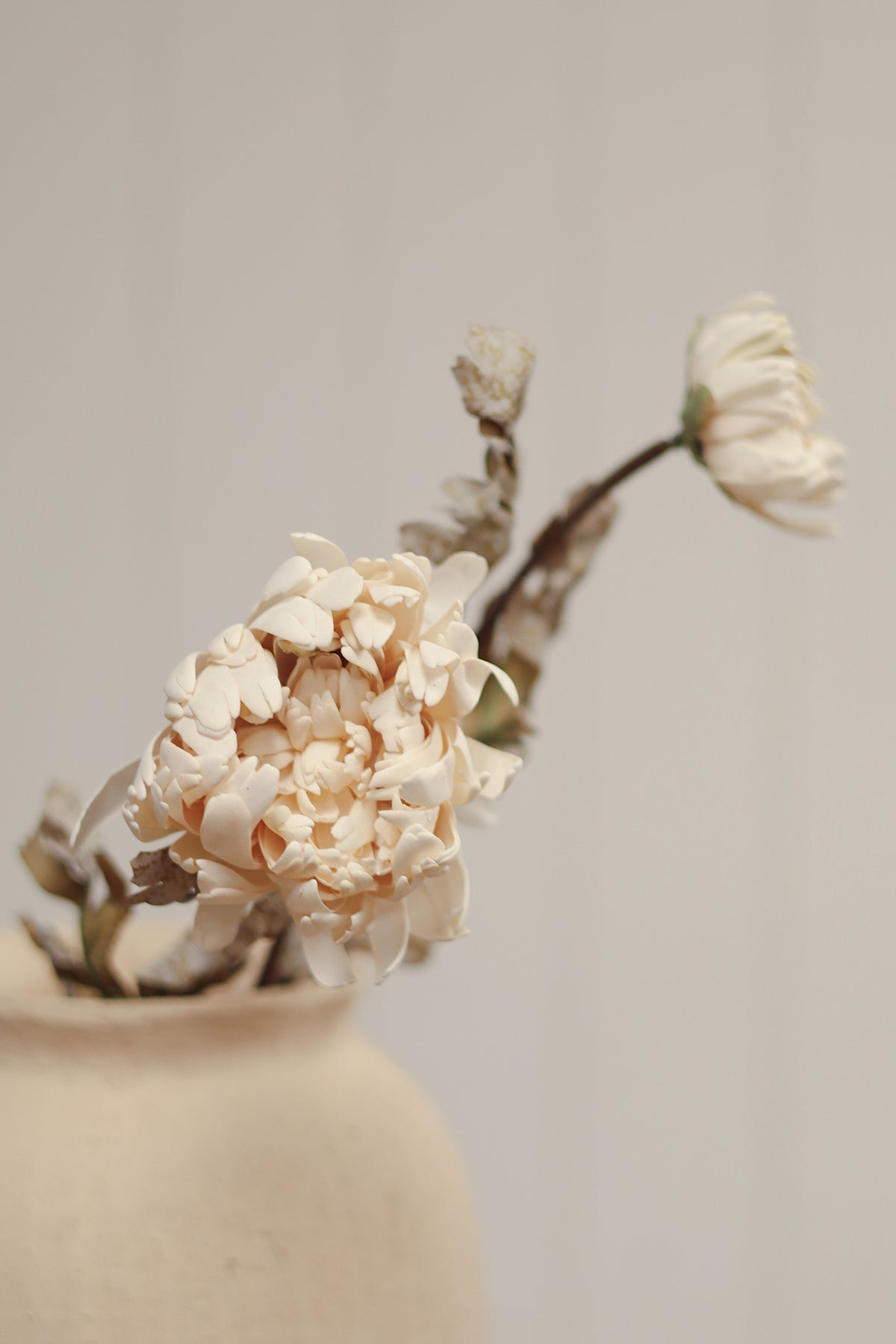 close-up on a vase with dahlia spray artificial cream colour flower stems with beige blooms and brown leaves arranged diagonally on a light wood grain surface at la maison garçonne in montreal.