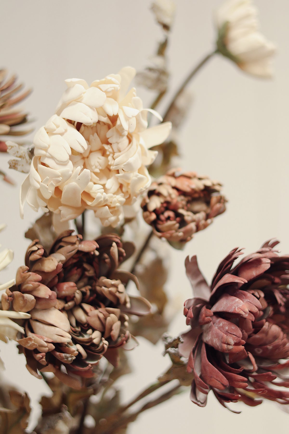 close-up on dahlia spray artificial cream colour flower stems with beige blooms and brown leaves arranged diagonally on a light wood grain surface at la maison garçonne in montreal.