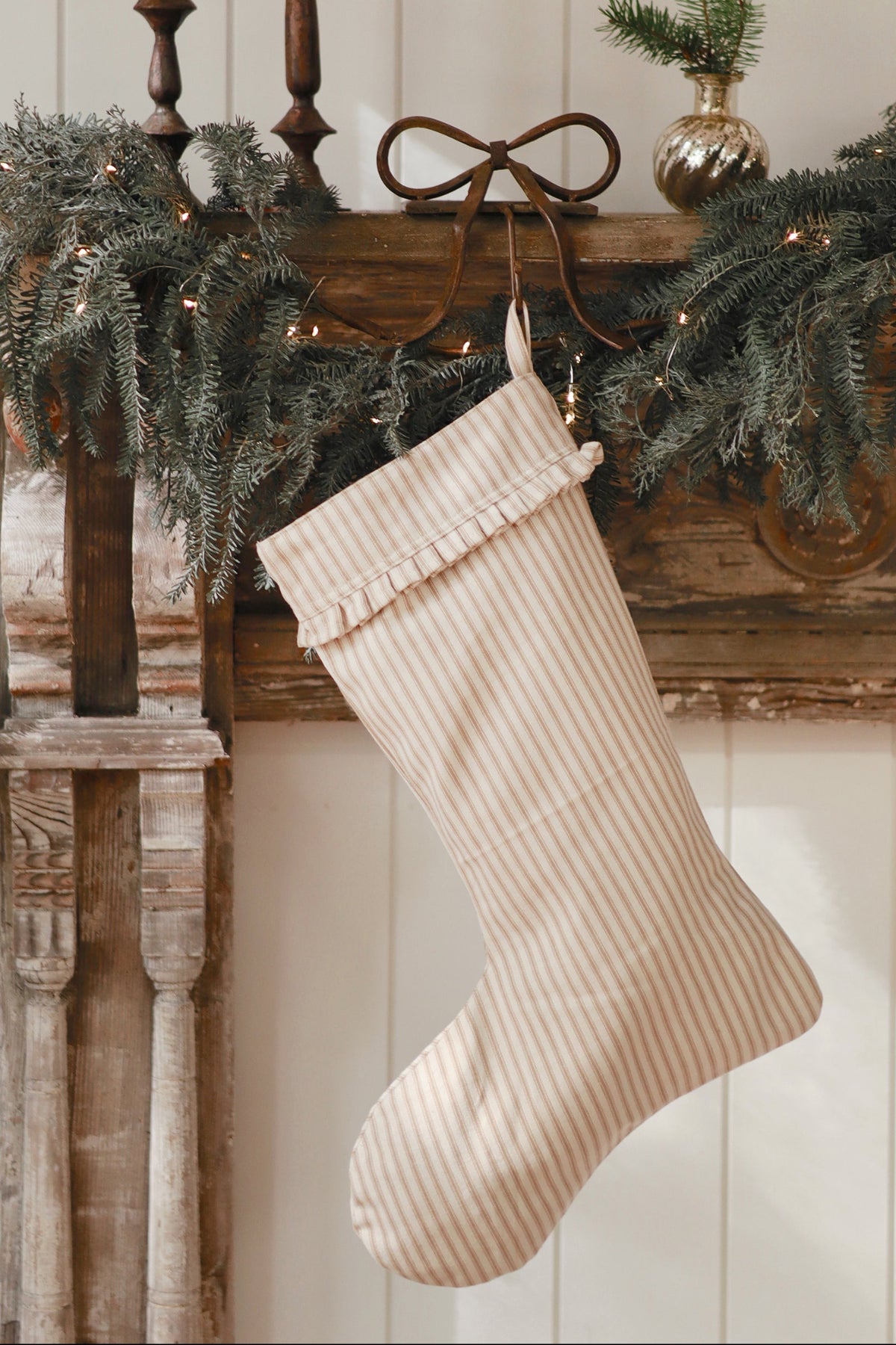 Beige Christmas stocking hanging on a wooden mantel with greenery and lights at la maison garçonne in montreal.