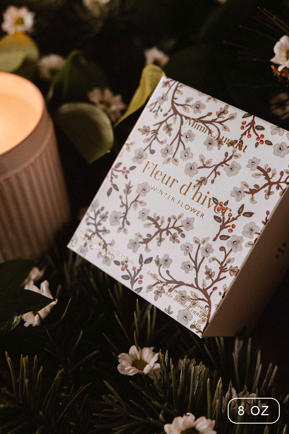 8oz Winter Flower Christmas Candle by Mimi and August with a decorative box on a bed of greenery and flowers