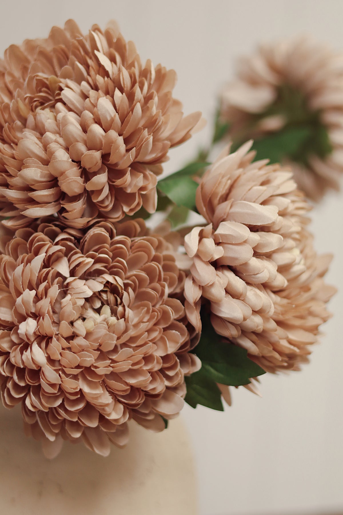 ultra close up on a beige vase with artificial beige chrysanthemum flowers stem with green leaves, at boutique la maison garçonne in montreal.