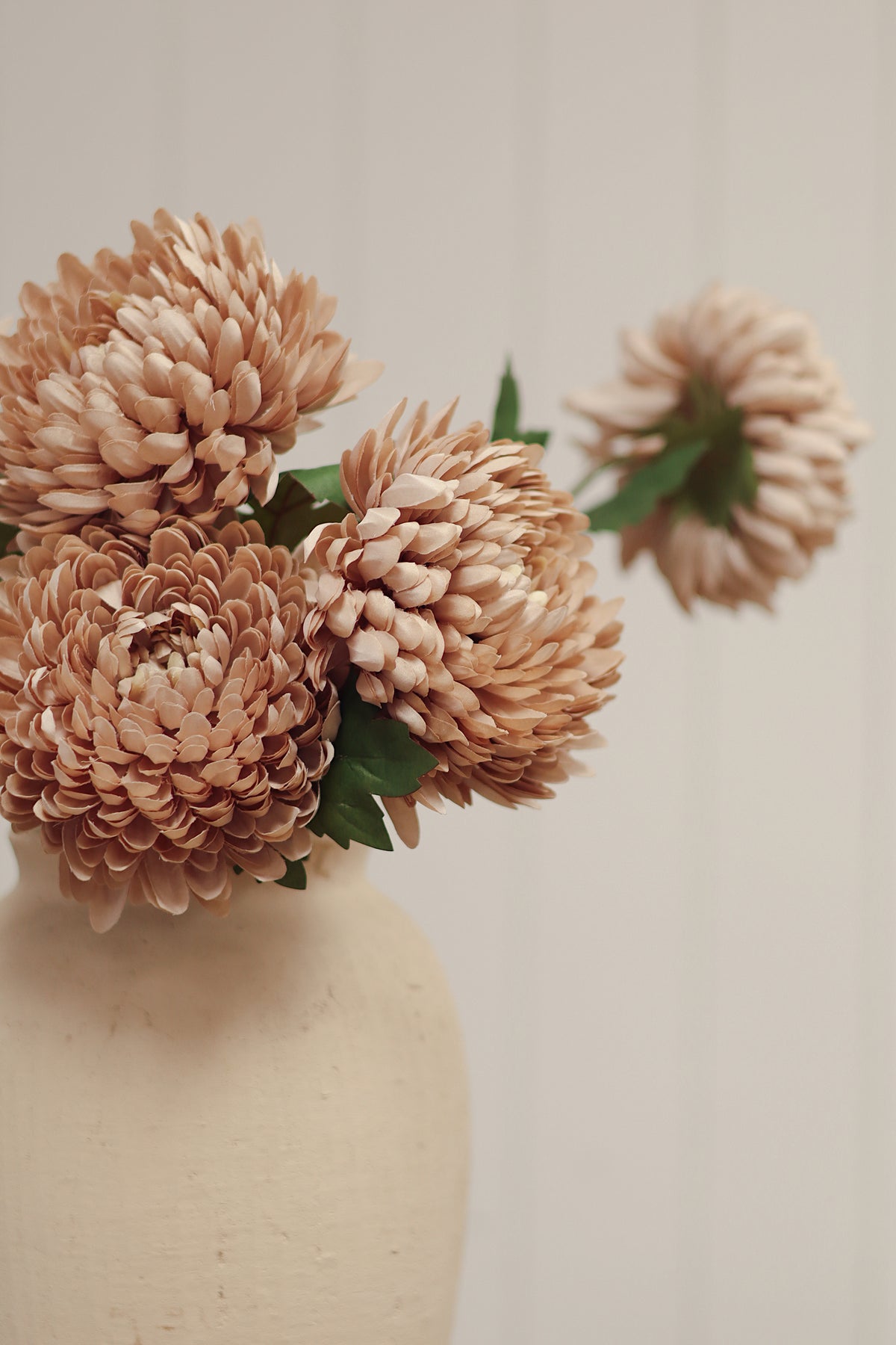 close up on a Beige vase with artificial beige chrysanthemum flowers stem with green leaves, at boutique la maison garçonne in montreal.