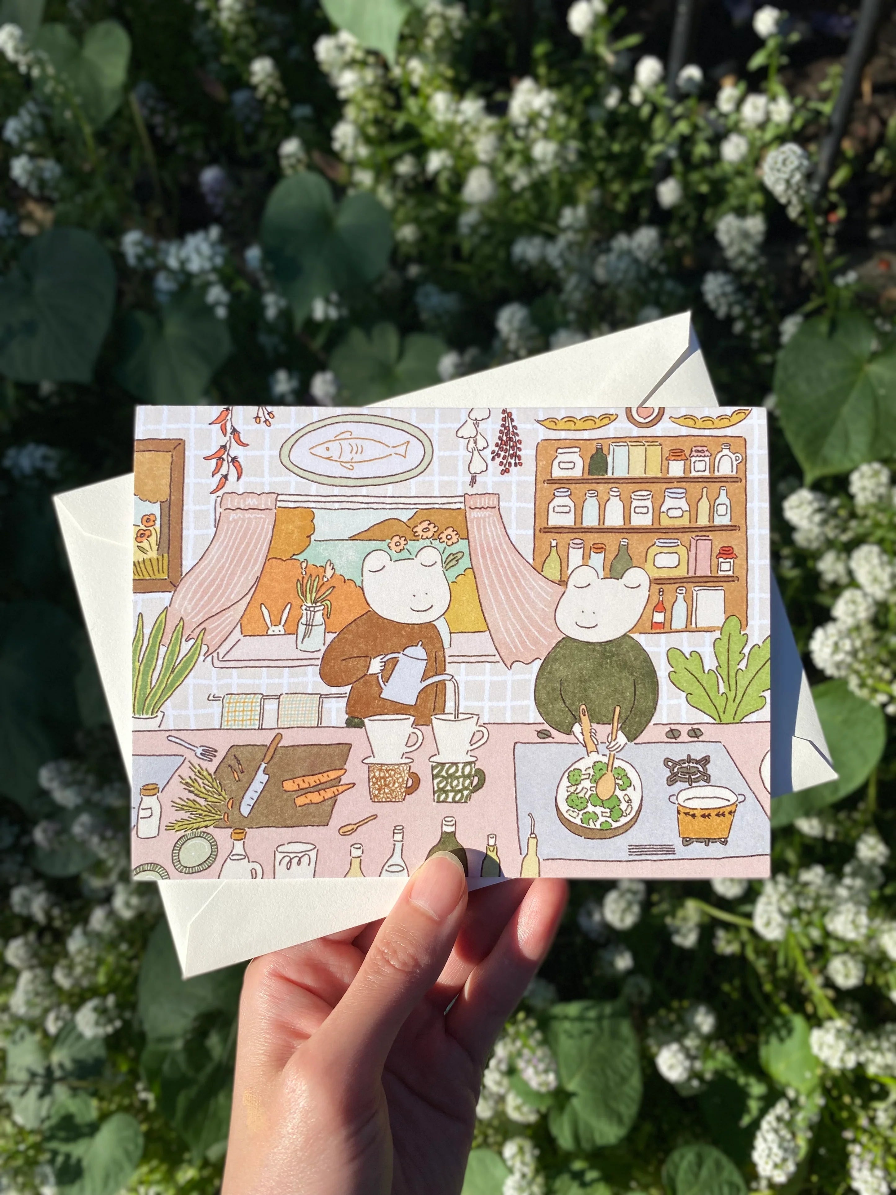 Illustration on a card of two frogs in a kitchen with various items on the counter.