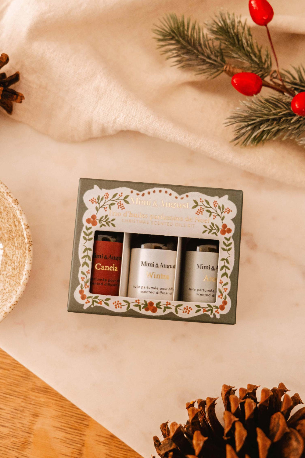 Christmas Scented Oils Trio by Mimi and August in a decorative box on a beige surface with Christmas decorations.