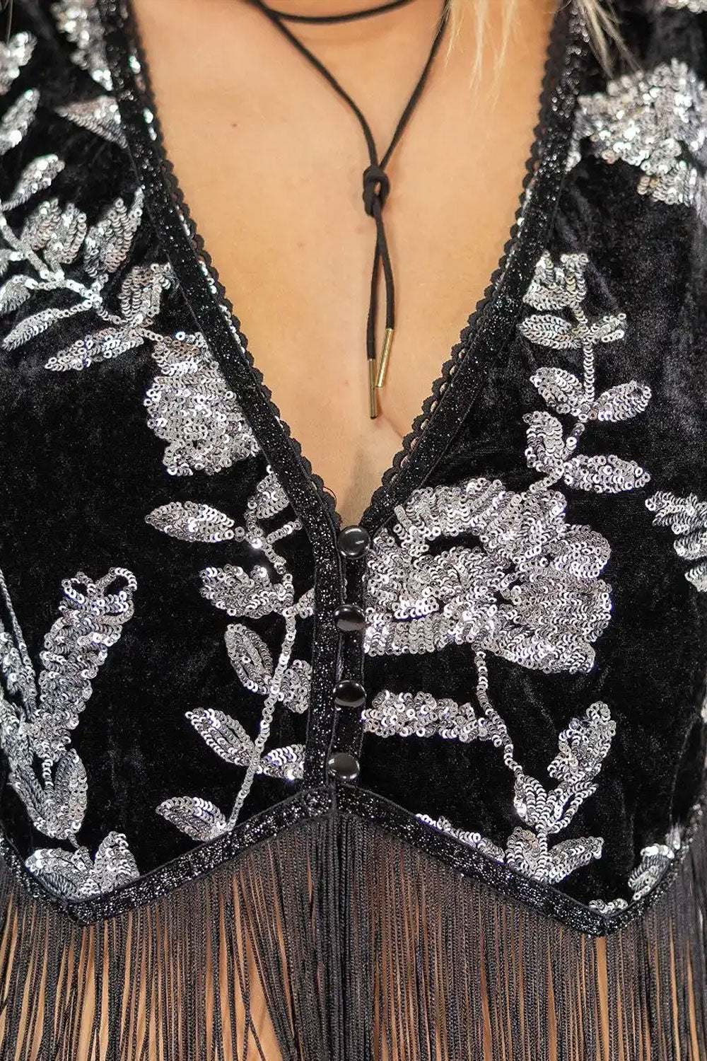 Close-up of a woman wearing a Black velvet dress with silver floral embroidery and fringe details.