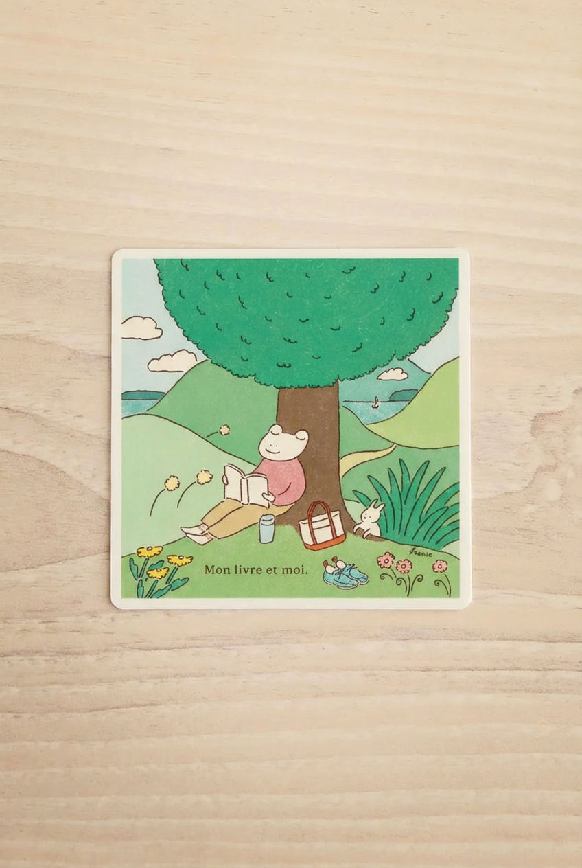 Illustration of a frog reading a book under a tree with a picnic basket and flowers with the text "my book and i".