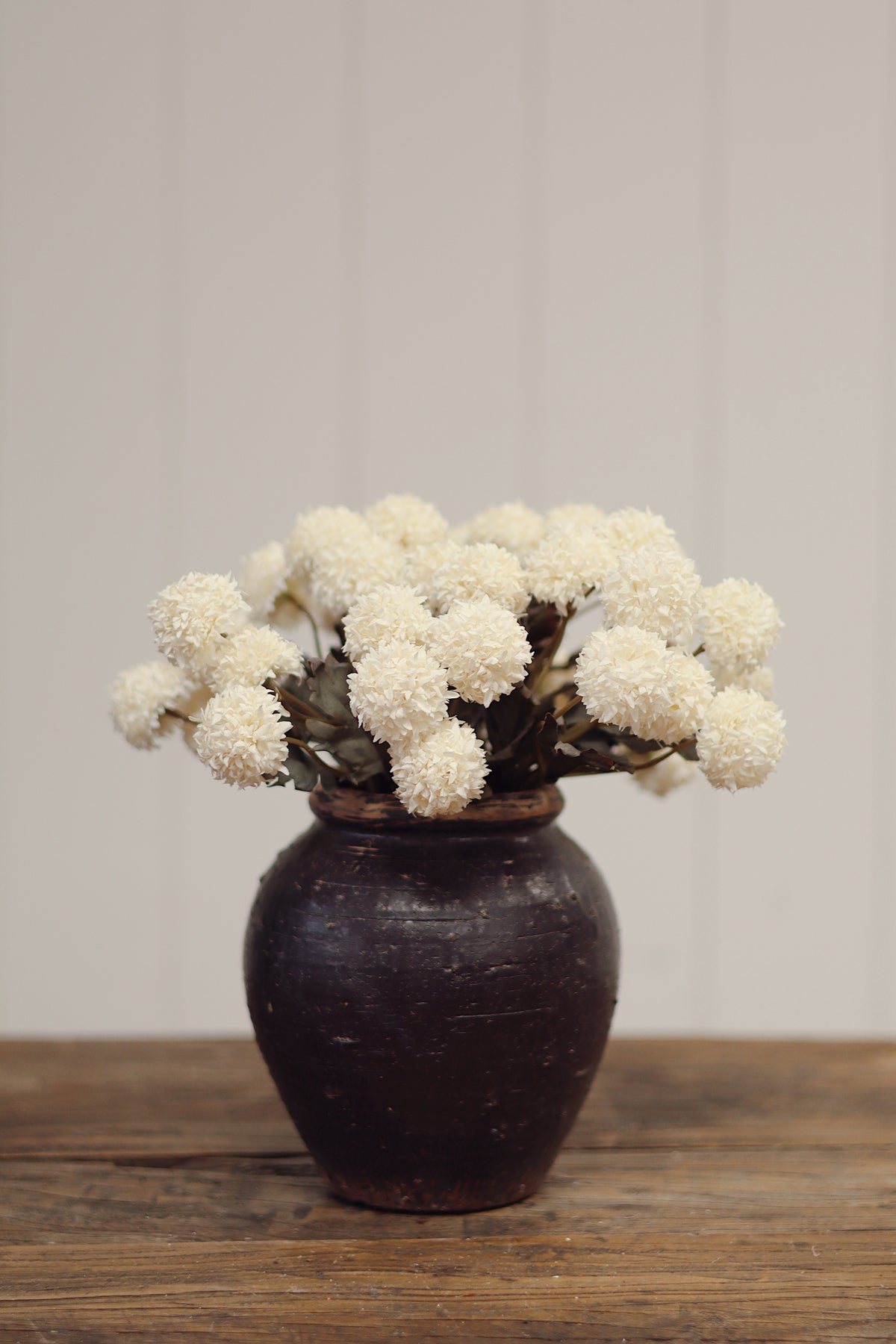Vintage dark brown vase with MORANDI IVORY artificial flowers on a wooden surface and light gray background at la maison garçonne montreal