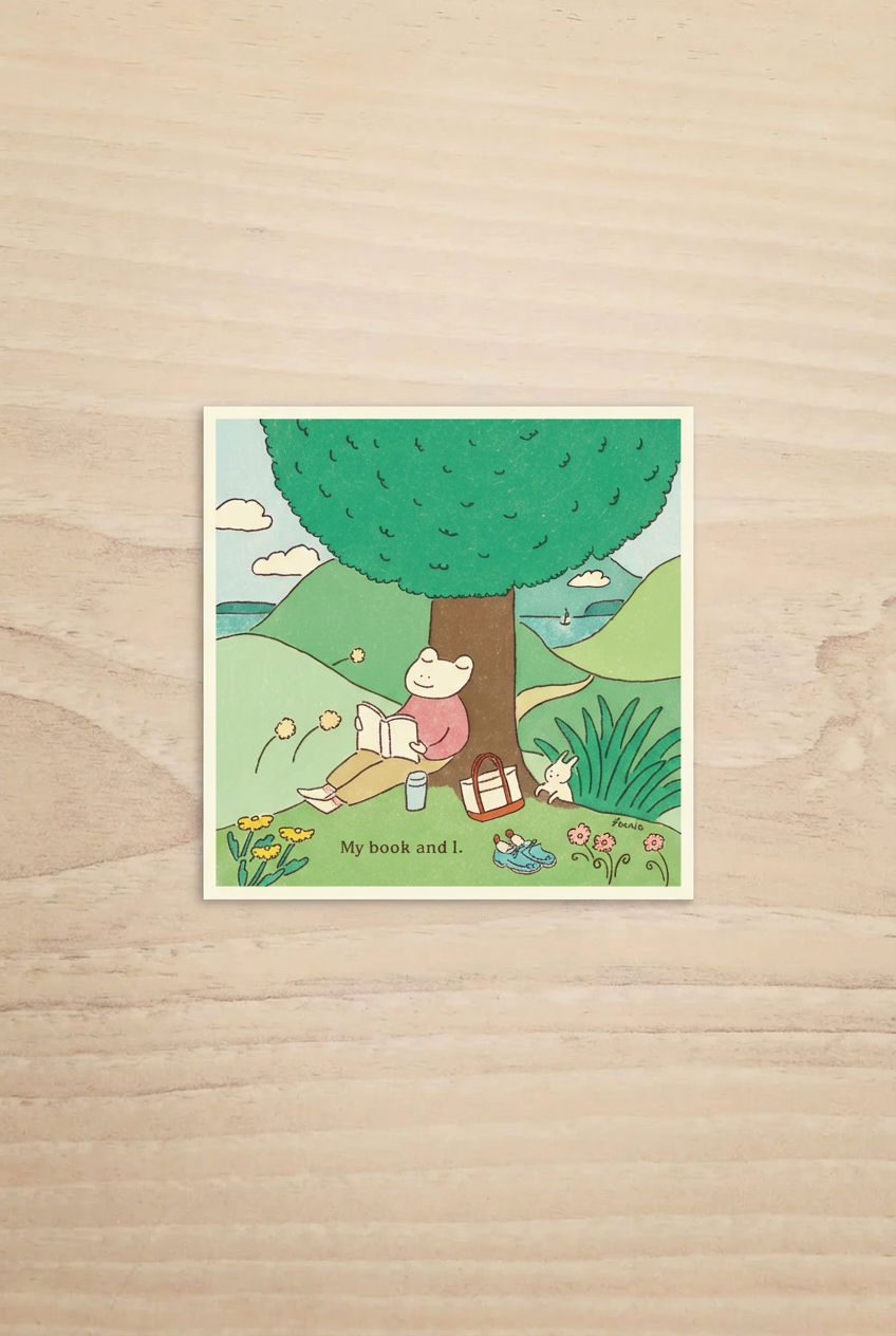 Illustration of a frog under a tree with a book with the text "My book and i" on a wooden surface.