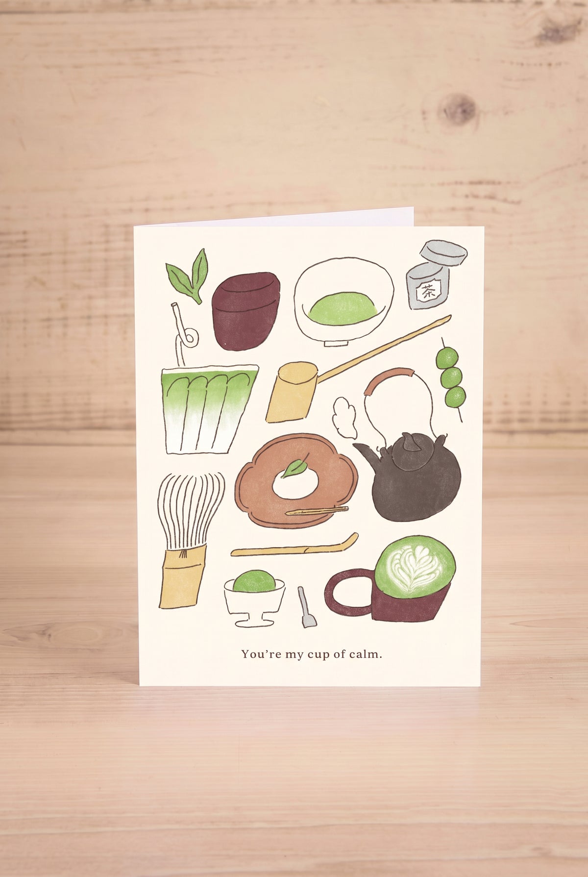 A 4.5 x 6" greeting card with a white background featuring hand-drawn illustrations from Foonie of Japanese matcha tea elements and the text 'You're my cup of calm.' at the bottom, displayed at la maison garçonne in Montreal