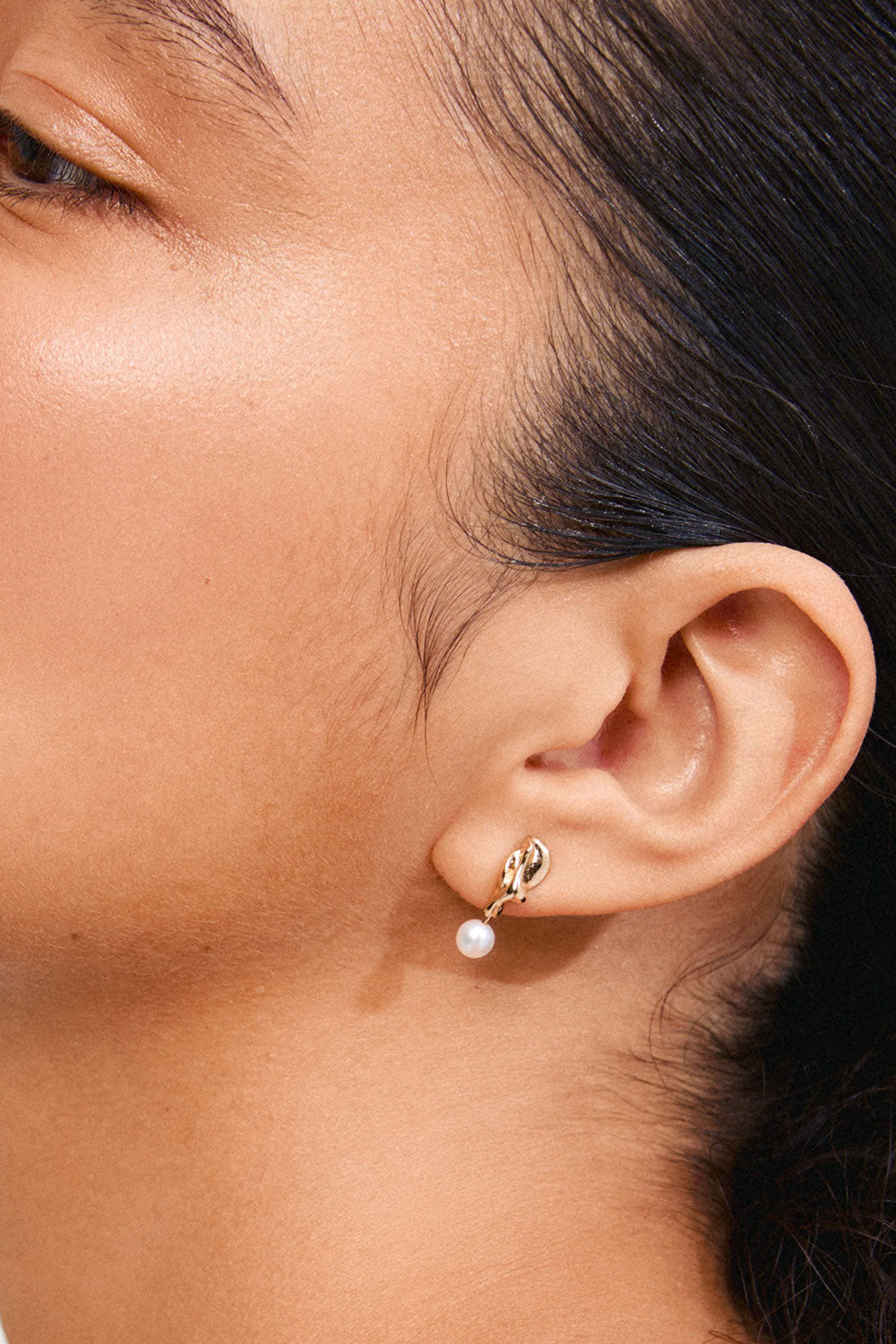 Close-up of an ear wearing Bogor from Pilgrim, a gold earring with a pearl available in Montreal