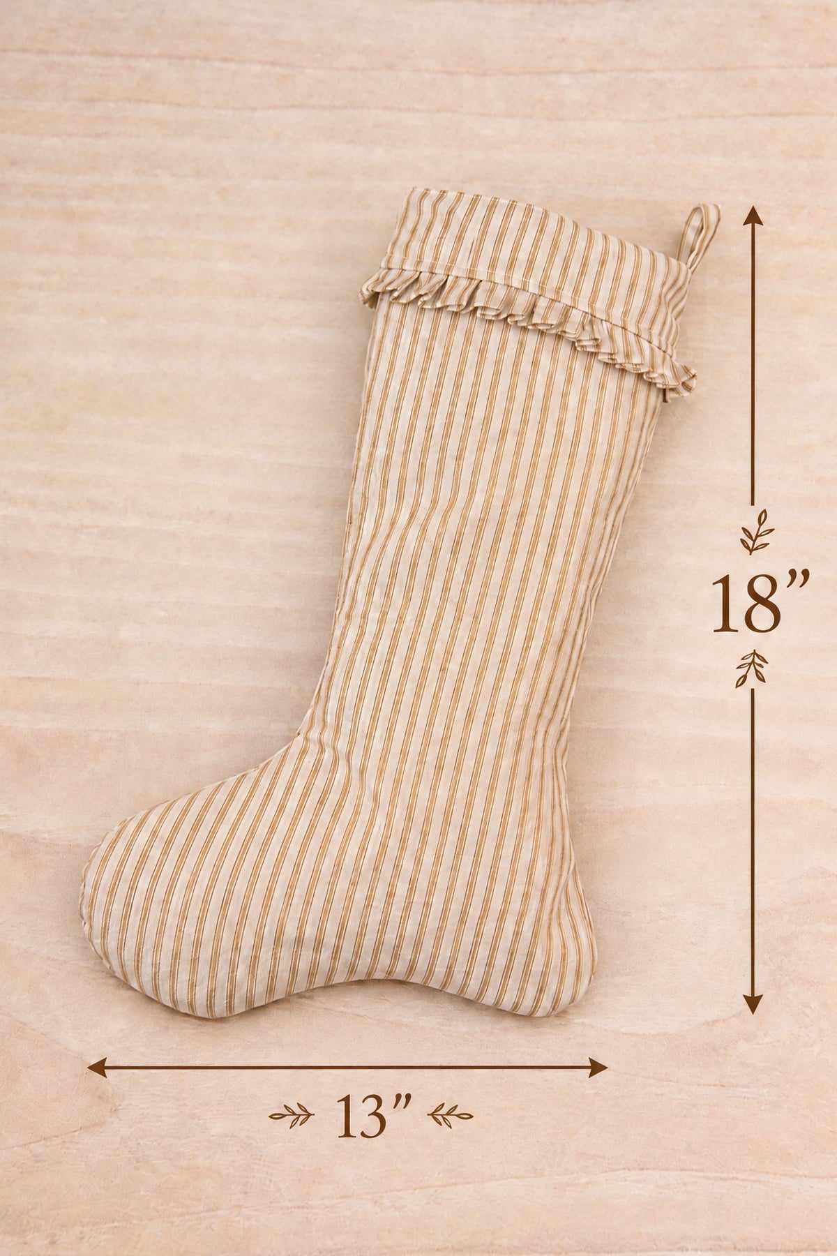 A small striped fabric Christmas stocking shown on a light wood surface at la maison garçonne in montreal with dimension arrows and labels indicating 13 inches wide and 18 inches tall.