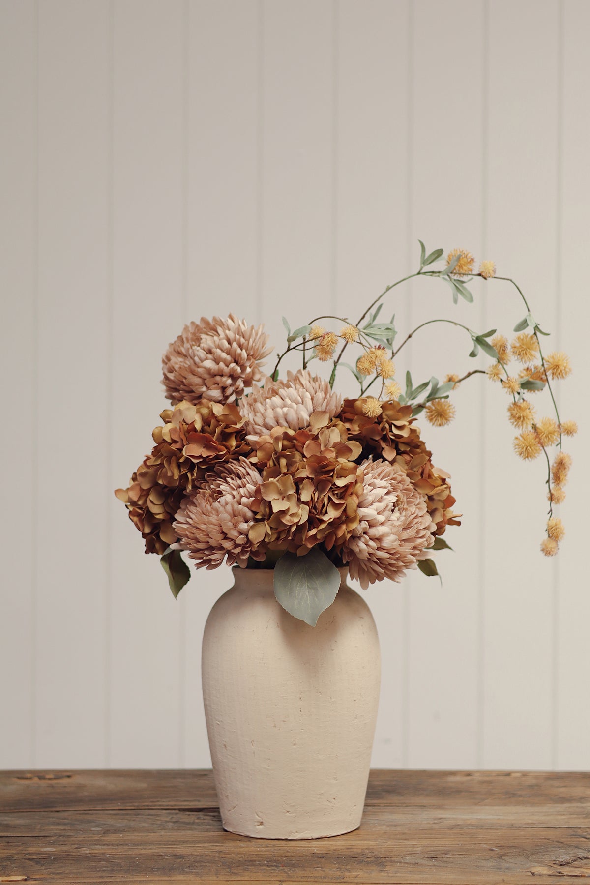 vase of mix flower including golden globe flower spray artificial flower stem with small yellow blossoms and muted green leaves, laid flat on a light wood surface at la maison garçonne boutique in montreal.