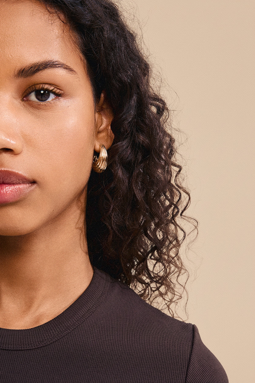 Close-up of a woman with curly hair wearing gold earrings from Pilgim