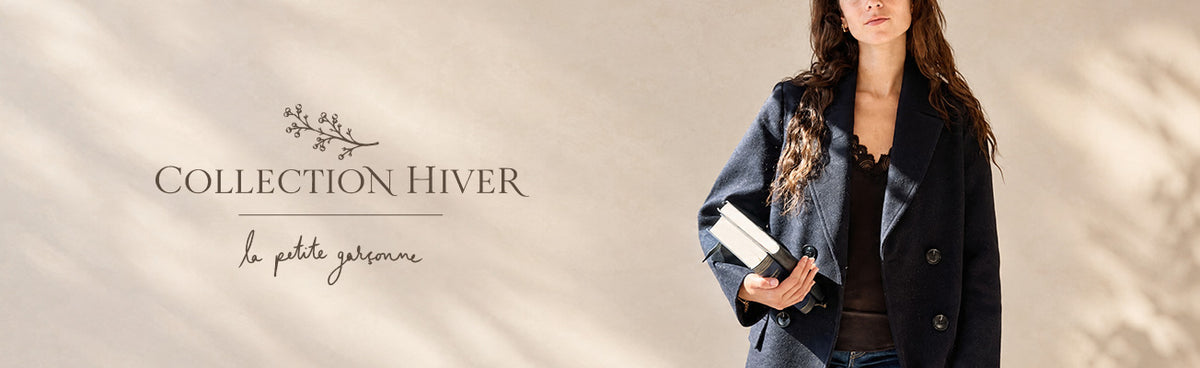 Une femme portant un manteau croisé bleu marine foncé et tenant un livre blanc, debout devant un fond beige chaleureux avec des ombres de feuilles. À gauche, on peut lire le texte « WINTER COLLECTION available at la petite garçonne in montreal ».