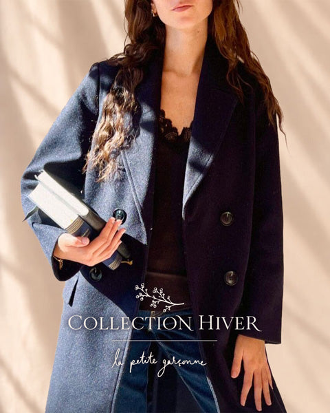 Une femme portant un manteau croisé bleu marine foncé par-dessus un haut noir, tenant une pochette noire. L’inscription « WINTER COLLECTION » apparaît sur un fond beige, présentant la collection d’hiver de La Petite Garçonne, boutique de vêtements pour femmes à Montréal.