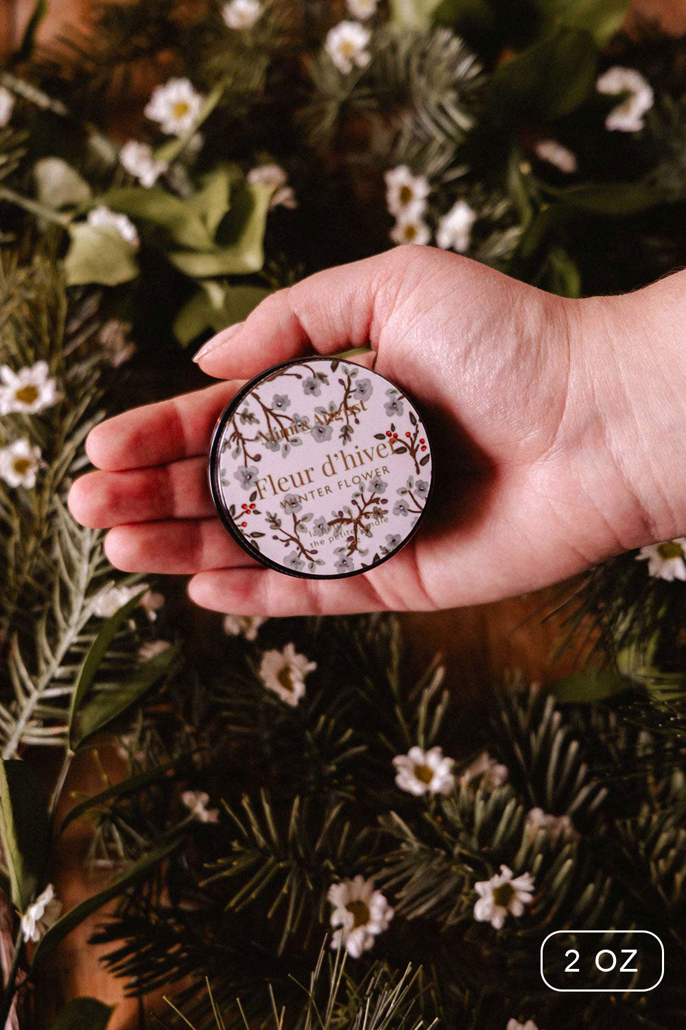2oz Winter Flower Christmas Candle by Mimi and August with a decorative box on a bed of greenery and flowers