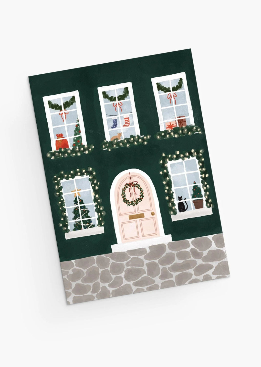 Christmas-themed greeting card from Mimi & August with a house facade, windows, and door decorated with lights and wreaths on a green background.