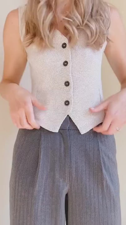 Video of a a mannequin is wearing the light gray vest Indio with dark buttons, standing against a plain beige background.